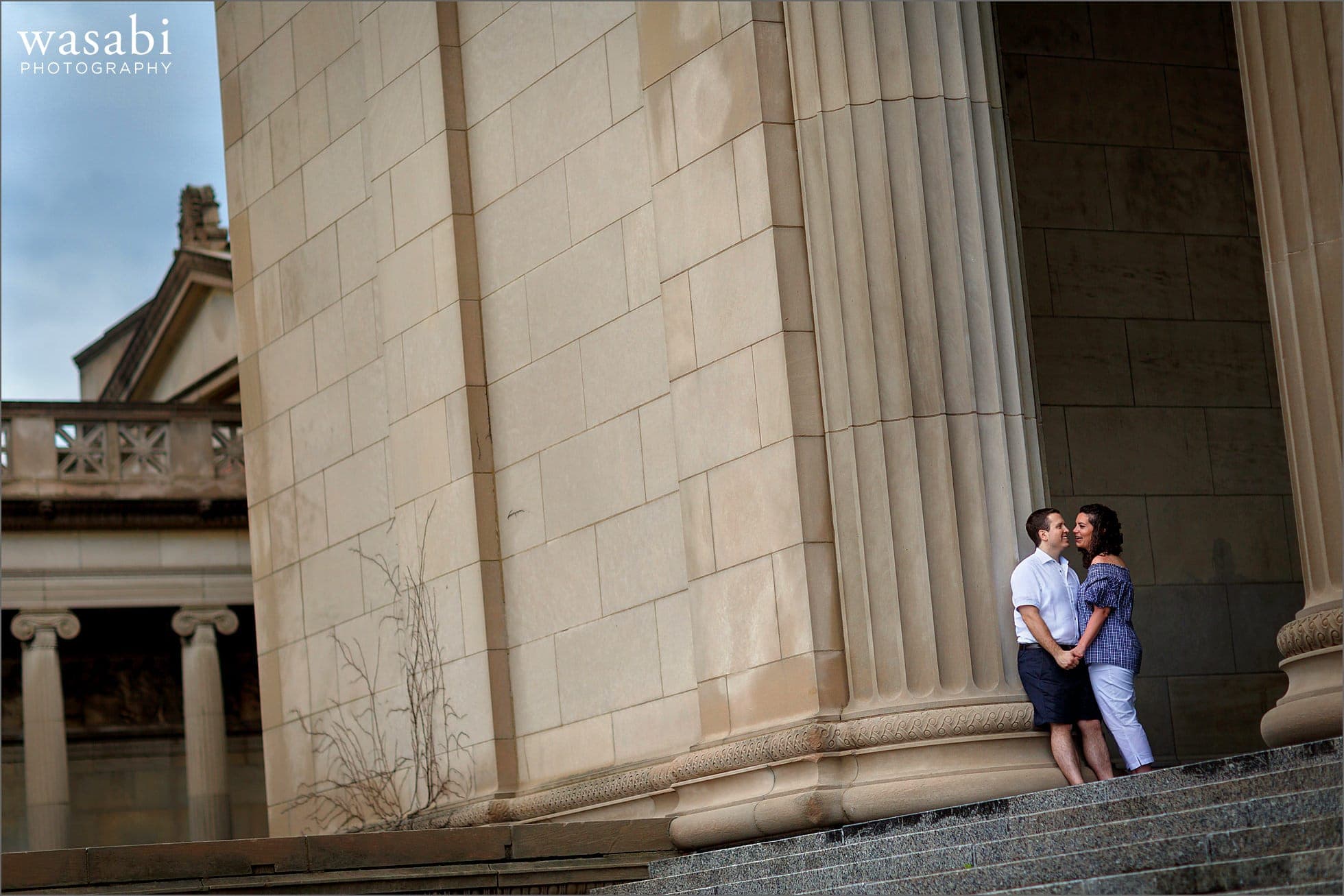 A couple laughs during their engagement session on the steps at The Museum of Science and Industry near Chicagos Jackson Park and Hyde Park neighborhood between Lake Michigan and The University of Chicago.