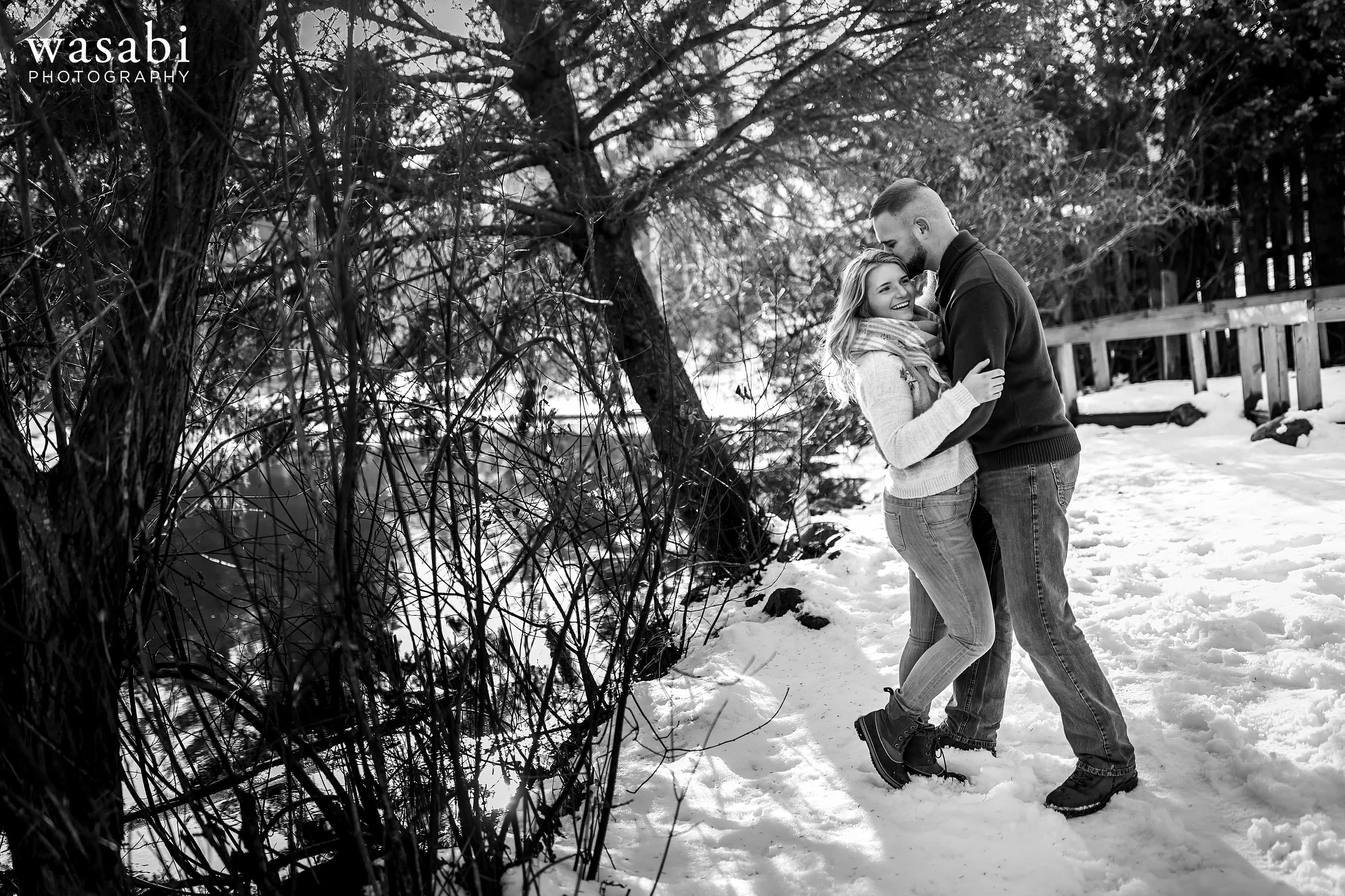 couple poses for engagement photo along a river during winter engagement session in Glen Arbor Michigan