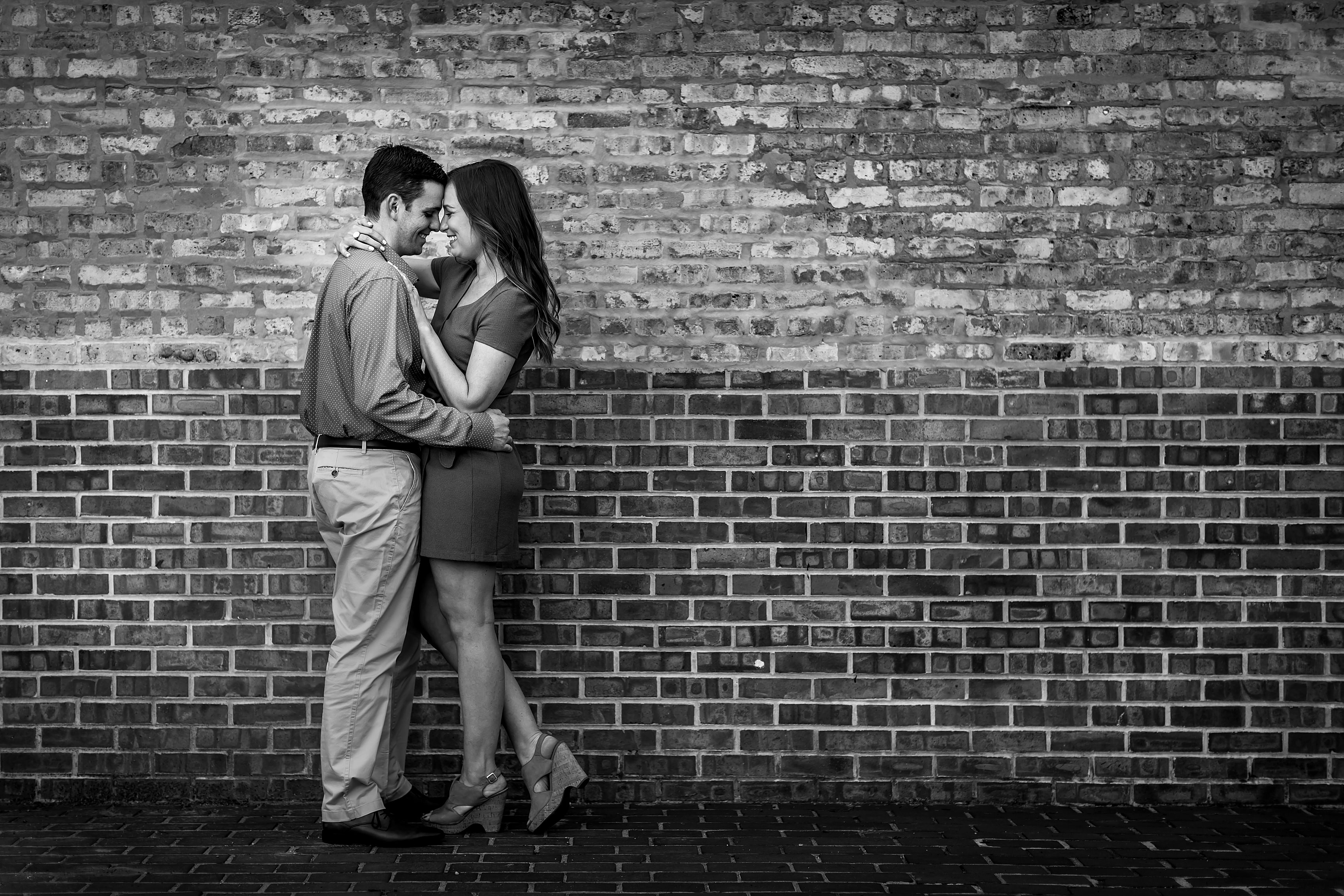 black and white photo of couple posing for engagement photos in Chicago's Old Town neighborhood in front of brick wall