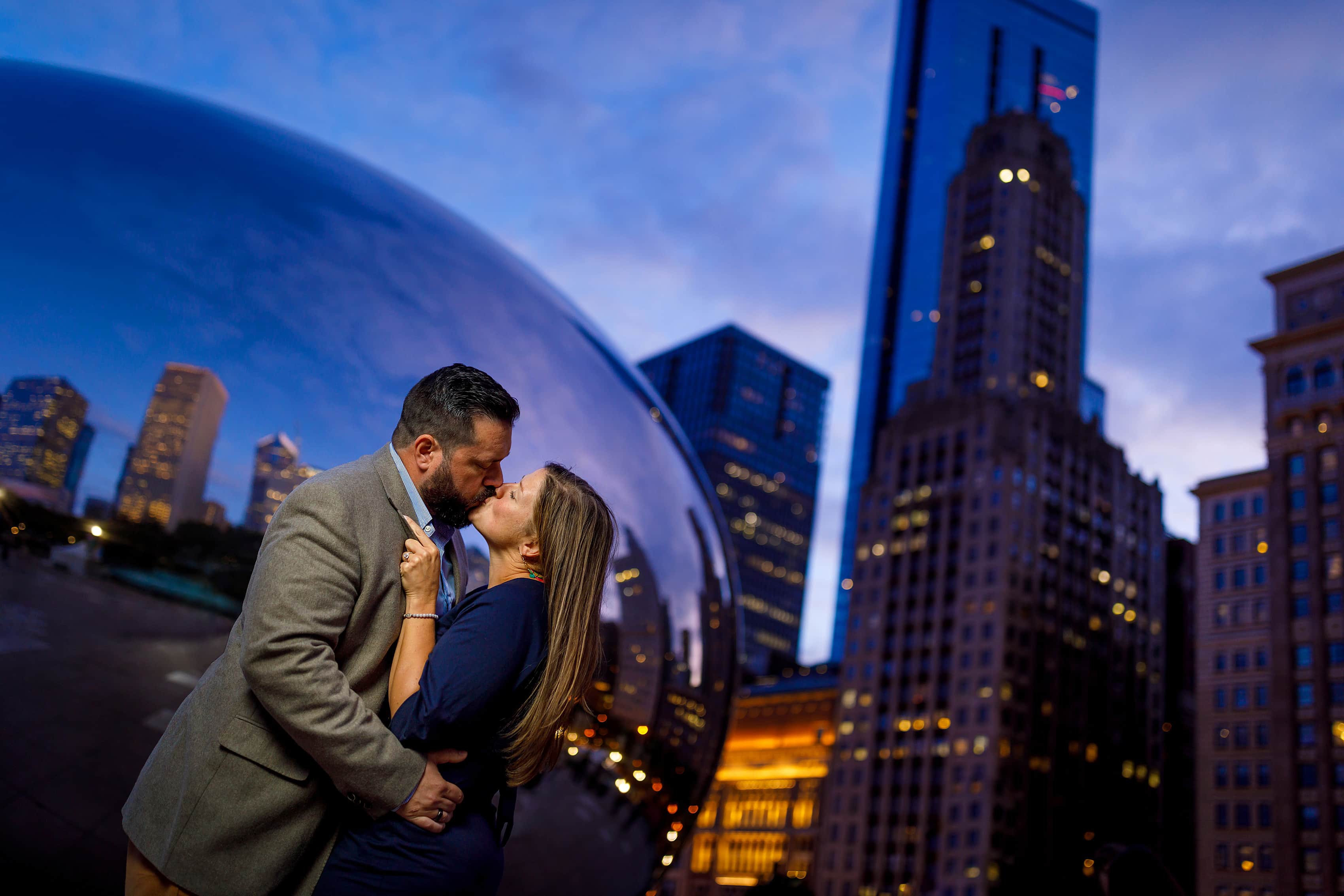 couple kisses during engagement session at Millennium Park with Cloudgate The Bean statue in the background and Chicago skyline