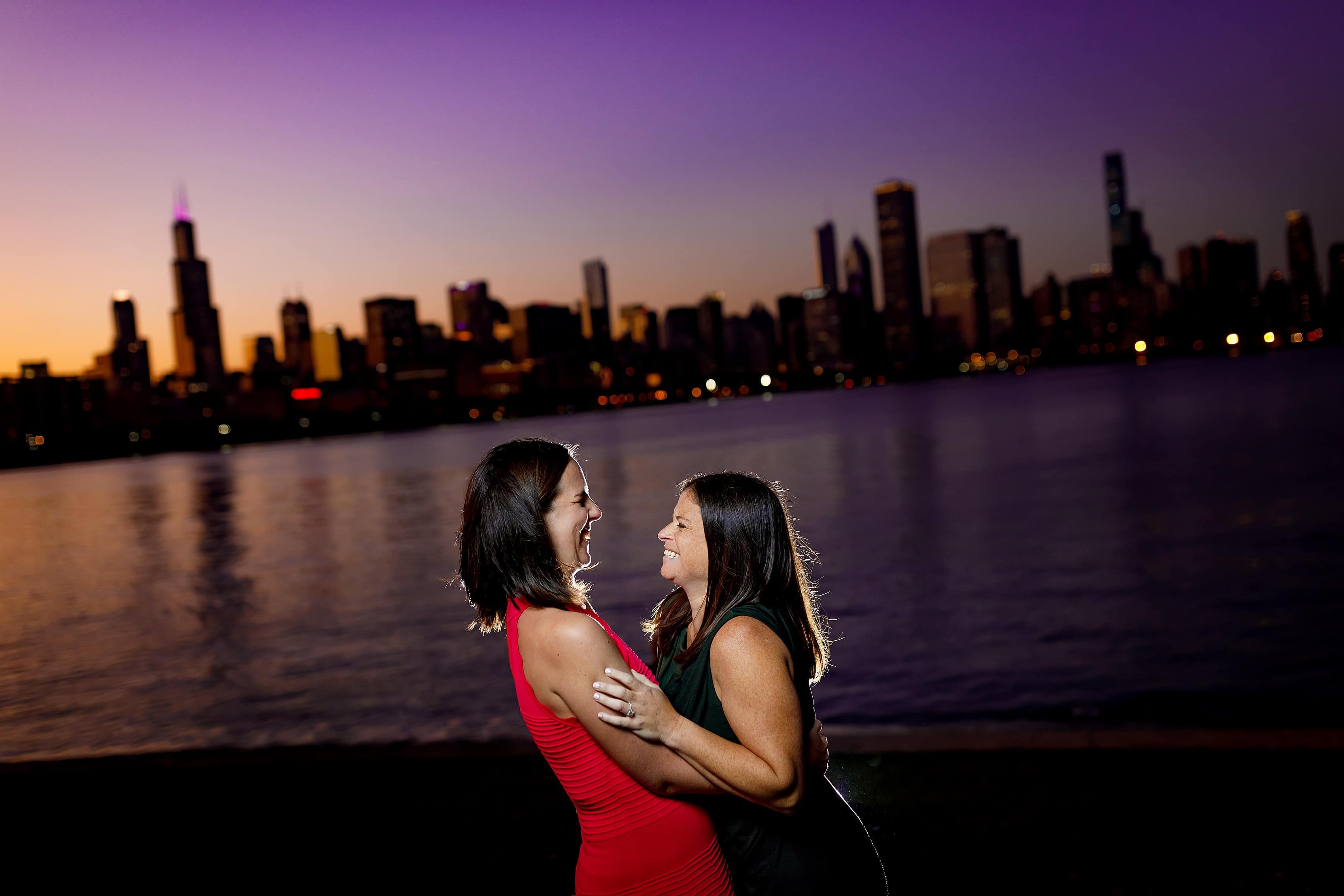 Couple laughs with skyline in the background during night engagement session at Adler Planetarium on Chicago's museum campus