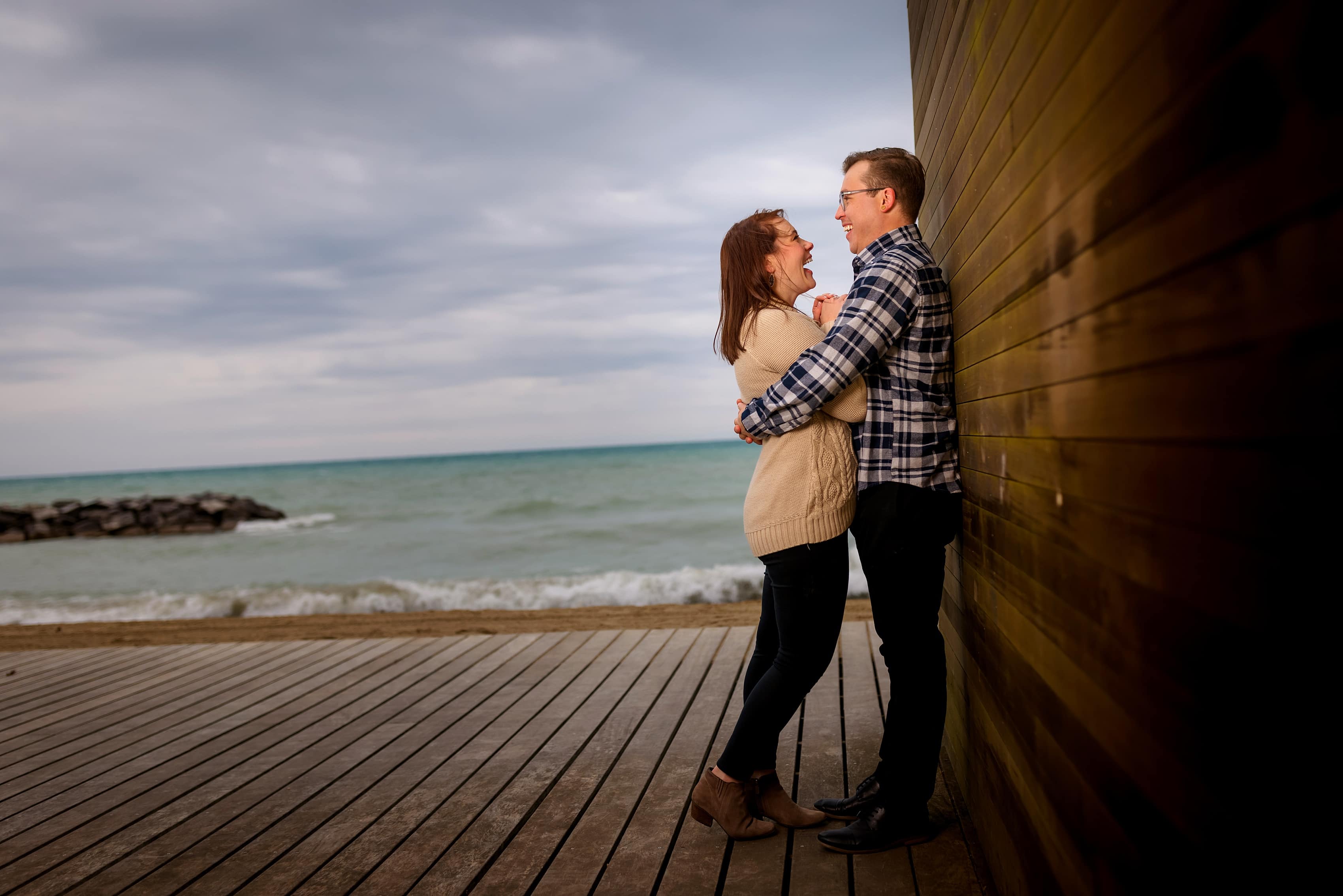 couple laughs on the beach during engagement session at Rosewood Beach in Highland Park, Illinois
