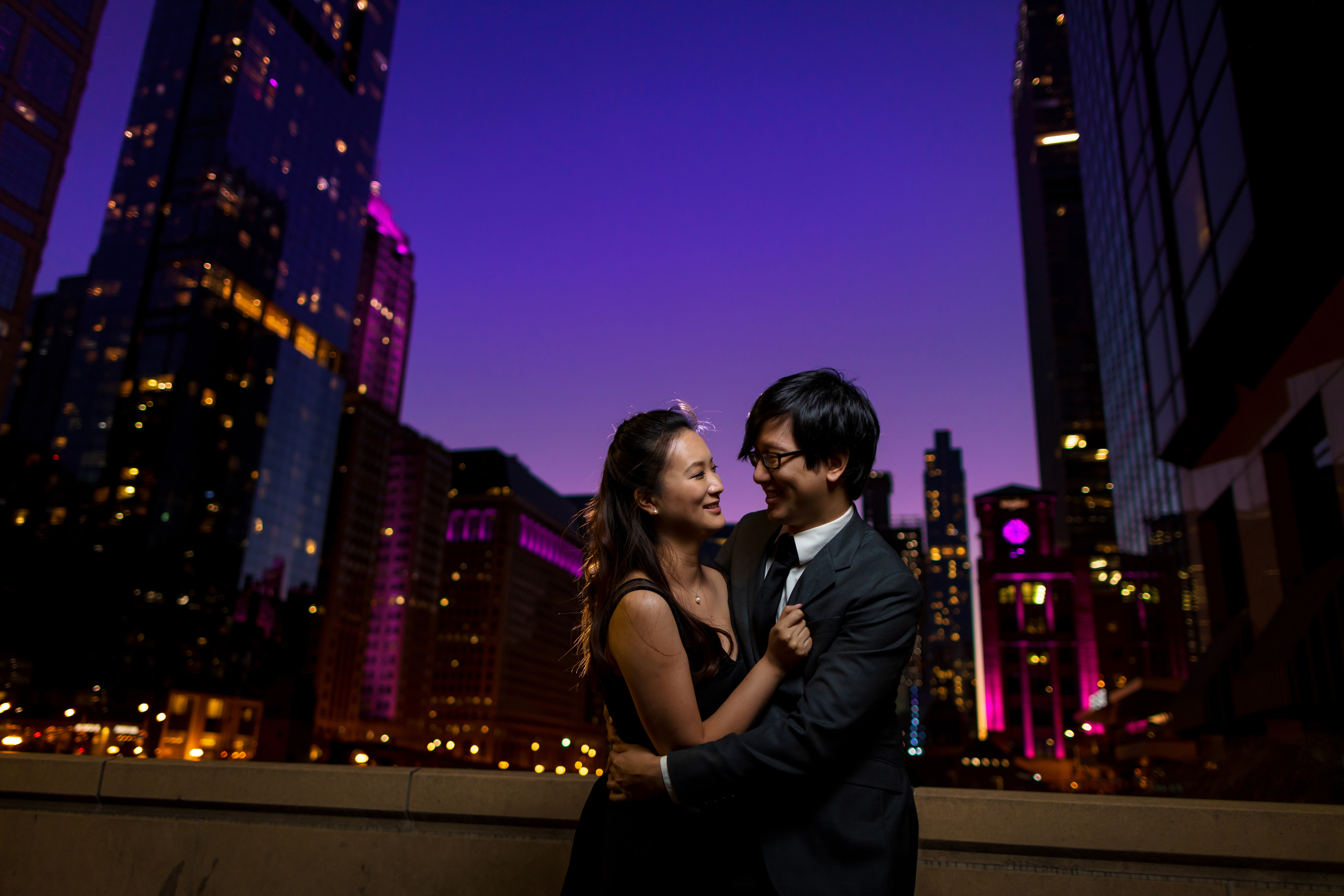 Couple poses for engagement photos at twilight in downtown Chicago with purple sky and buildings lit up