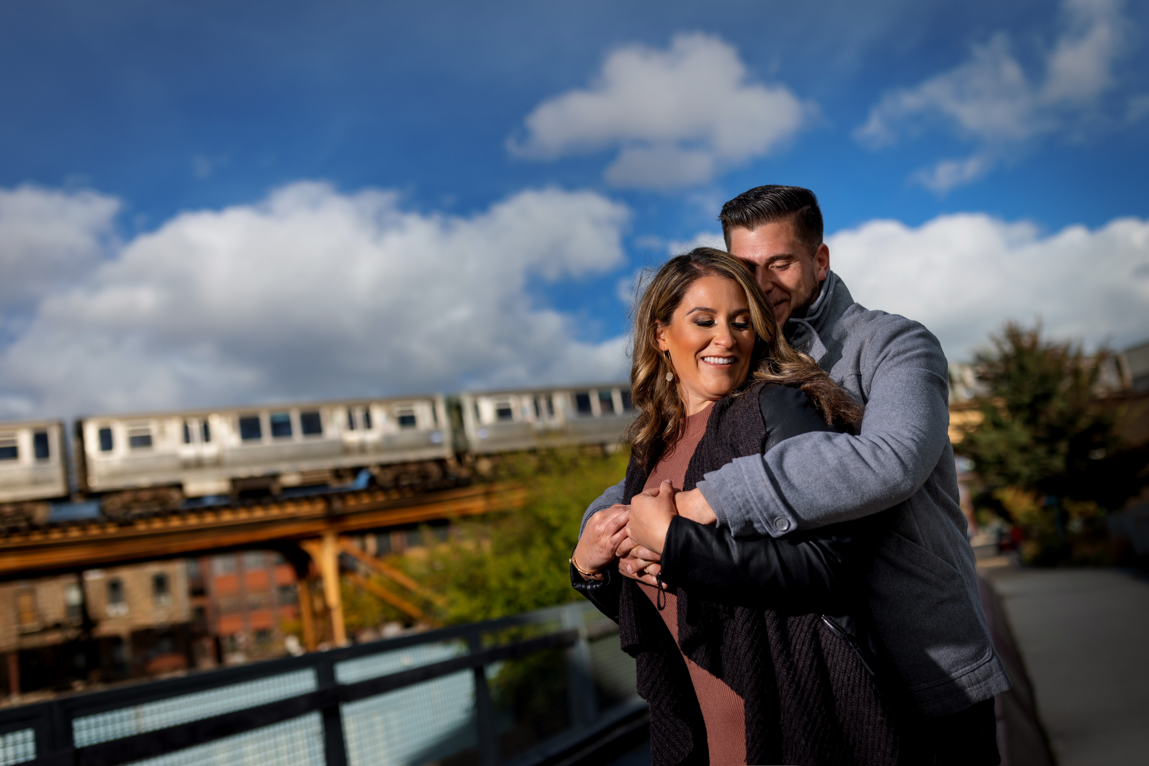 couple poses for engagement photos on the 606 trail in Chicago's Wicker Park neighborhood with the El train in the background