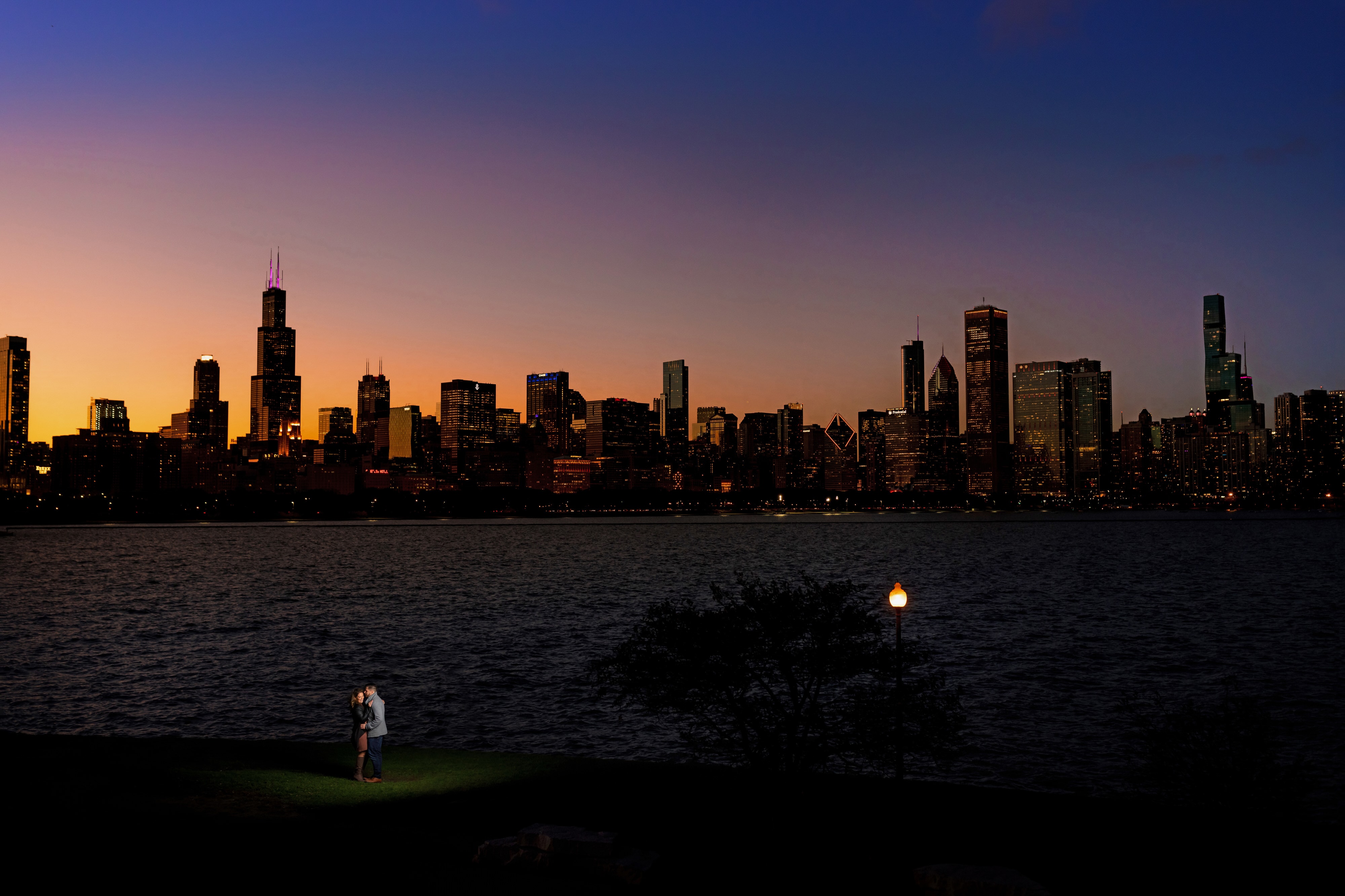 couple poses for engagement photos at Adler Planetarium with the Chicago skyline in the background