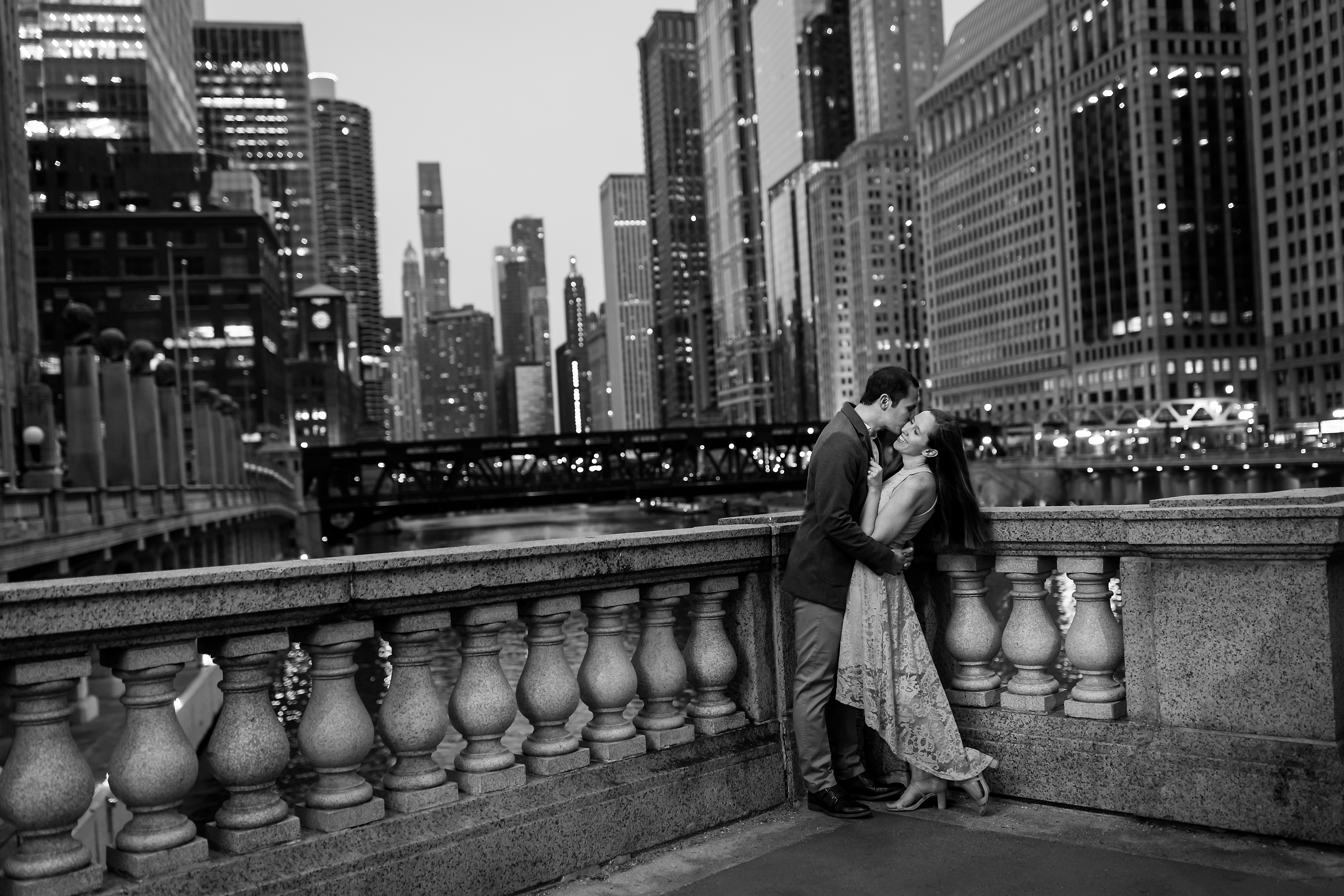 Wedding couple poses for engagement photos with Chicago skyline in the background during twilight