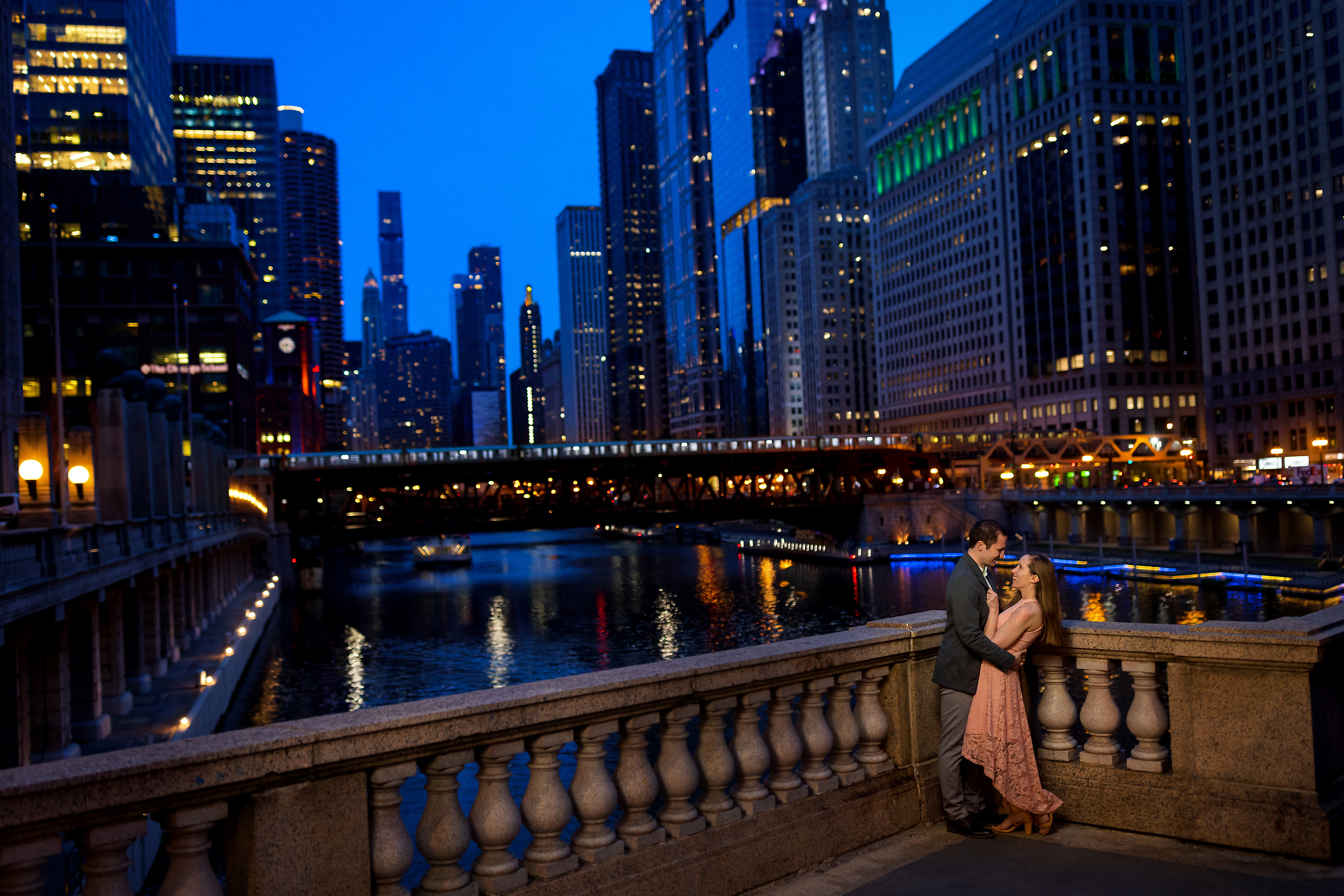 Wedding couple poses for engagement photos with Chicago skyline in the background during twilight