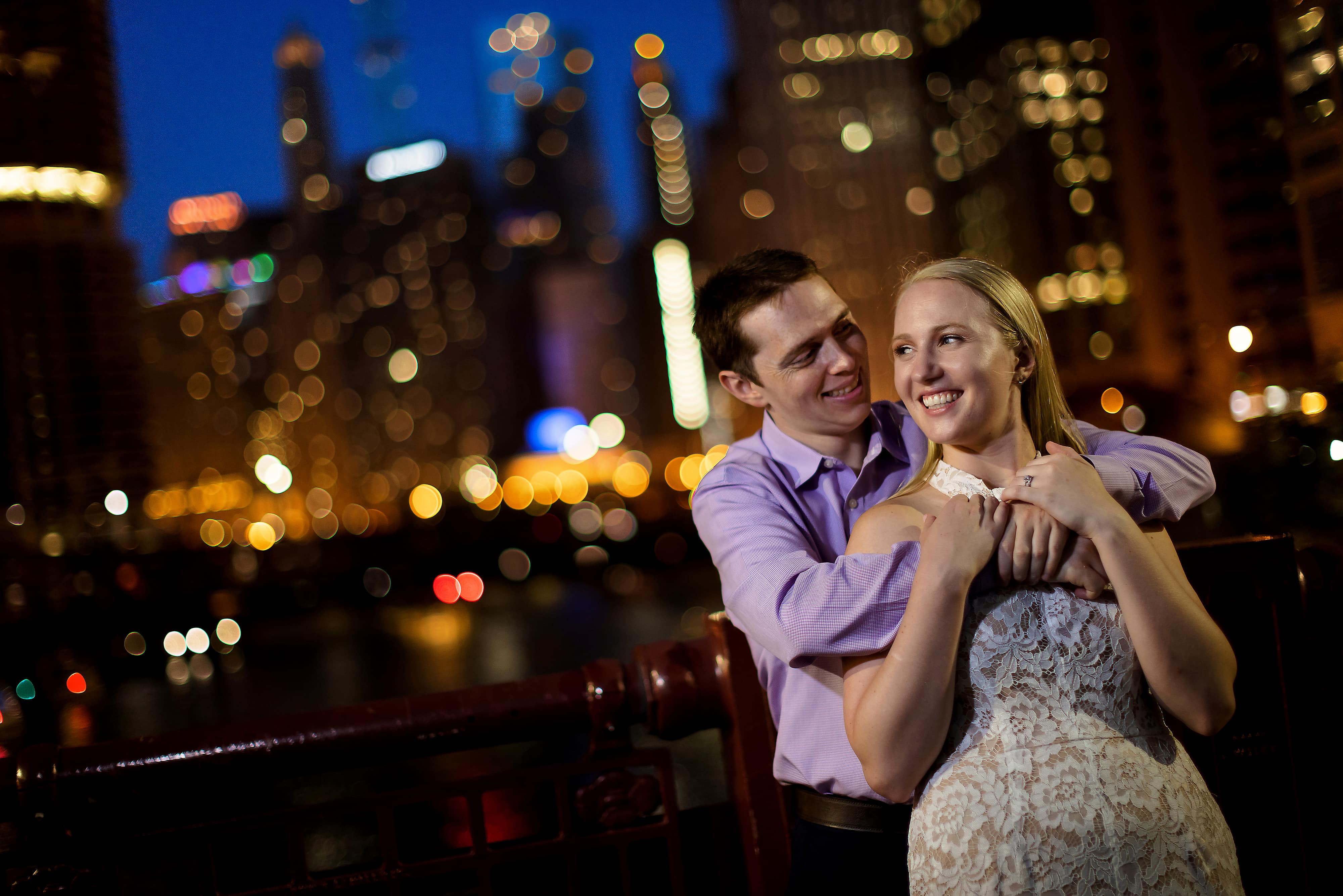 couple poses for photos on LaSalle Street Bridge during summer engagement session at night in downtown Chicago
