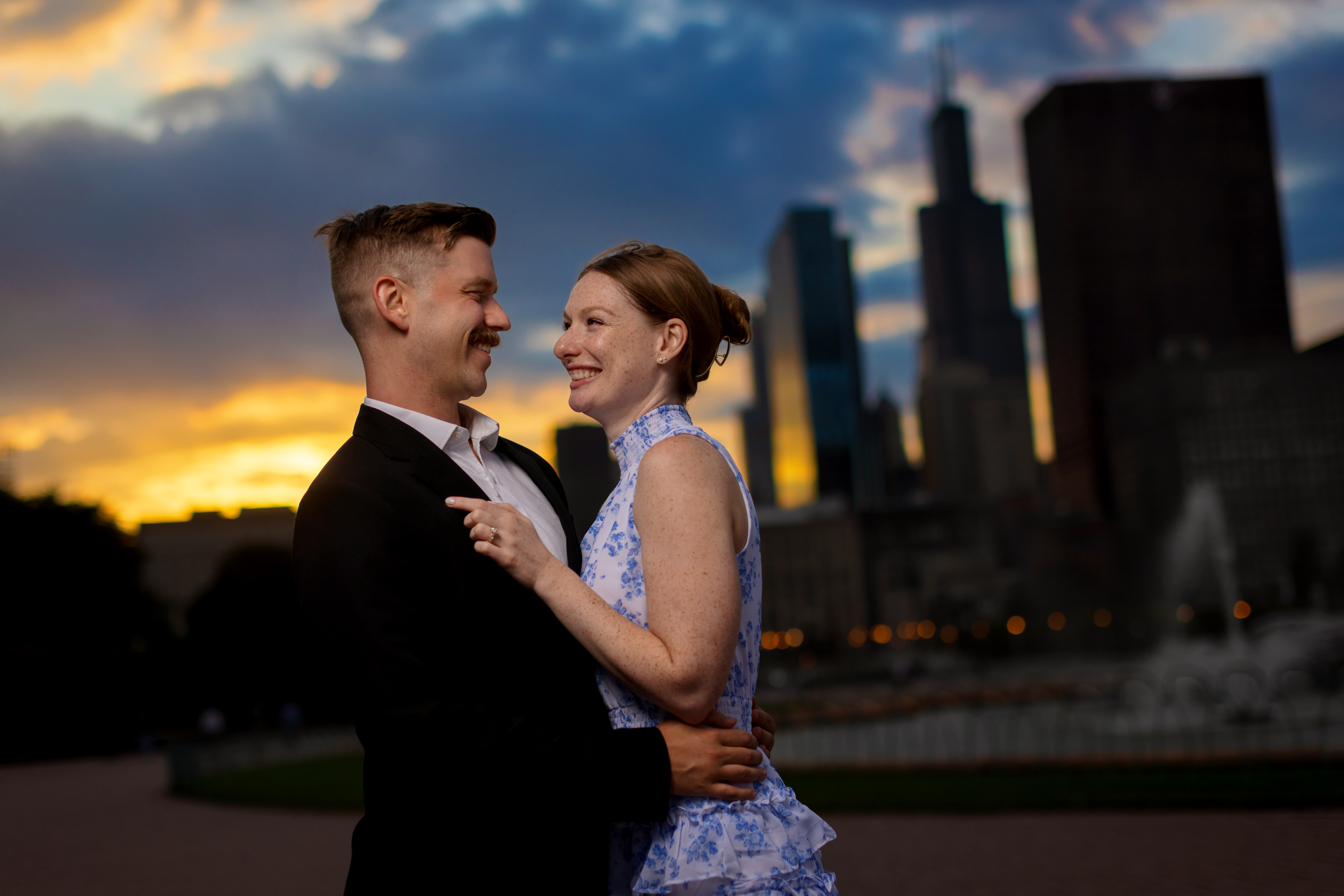 Couple poses for photos together in front of Buckingham Fountain during downtown engagement session at sunset