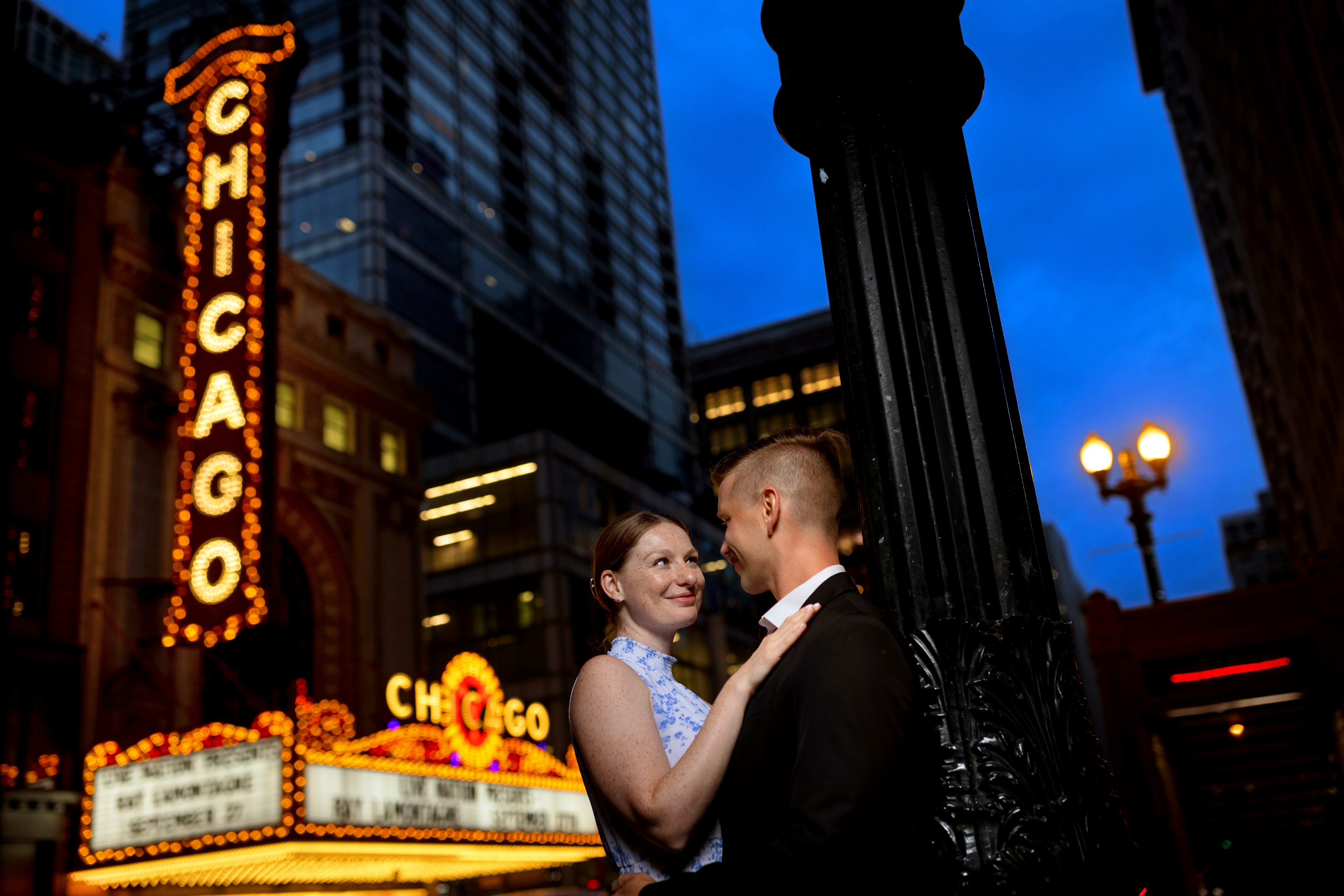 Couple poses for photo in front of Chicago Theatre sign at dusk during downtown engagement session