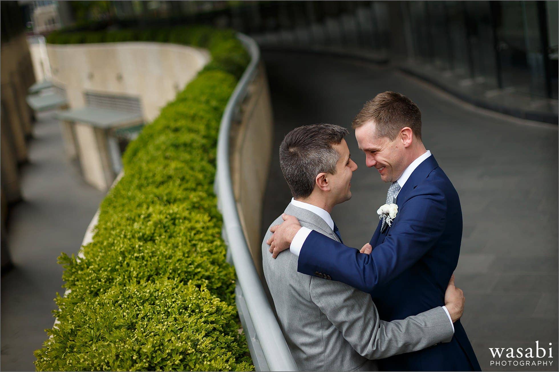 two grooms embrace on a sidewalk near Trump Tower in downtown Chicago on their wedding day