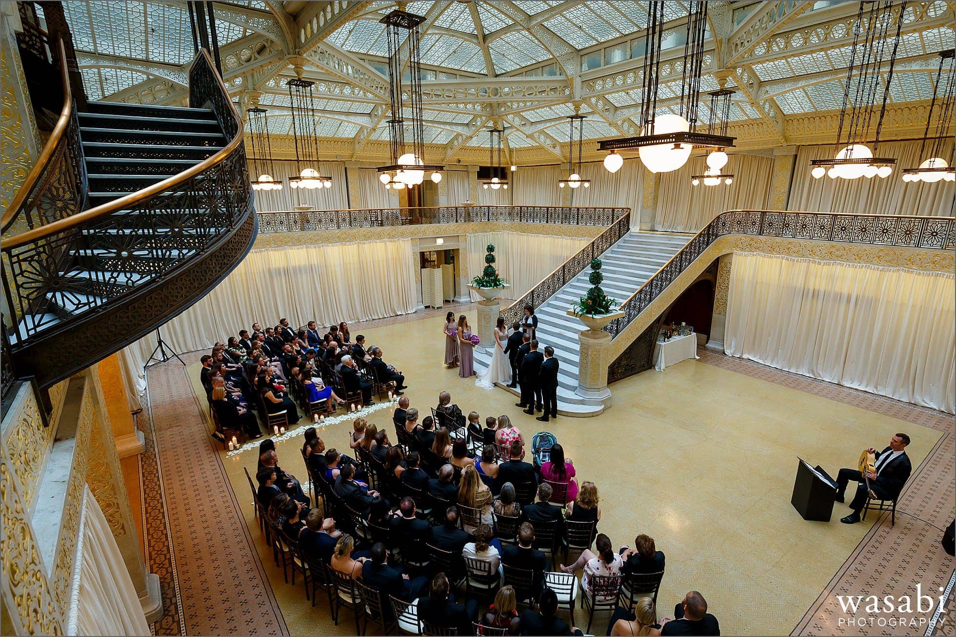 The Rookery Building wedding photos wide angle full room view of wedding ceremony at The Rookery Building in Chicago with stairs in the forground and steps in the background