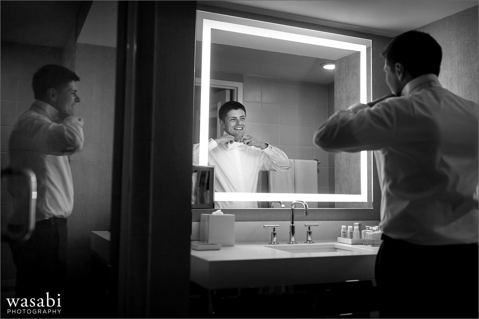 groom ties bowtie in reflection mirror while getting ready for his wedding at Renaissance Chicago Downtown Hotel