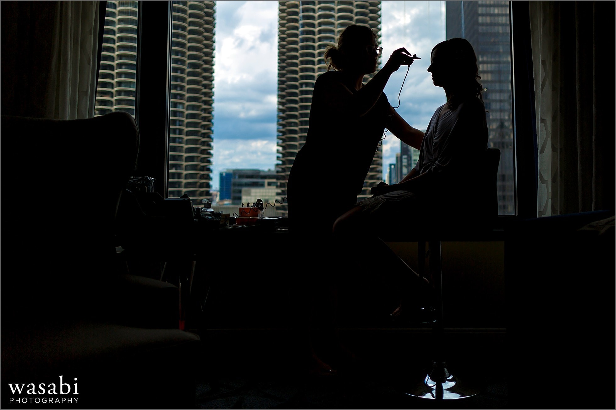 silhouetted bride gets her makeup airbrushed on while getting ready at Renaissance Chicago Downtown Hotel for her wedding