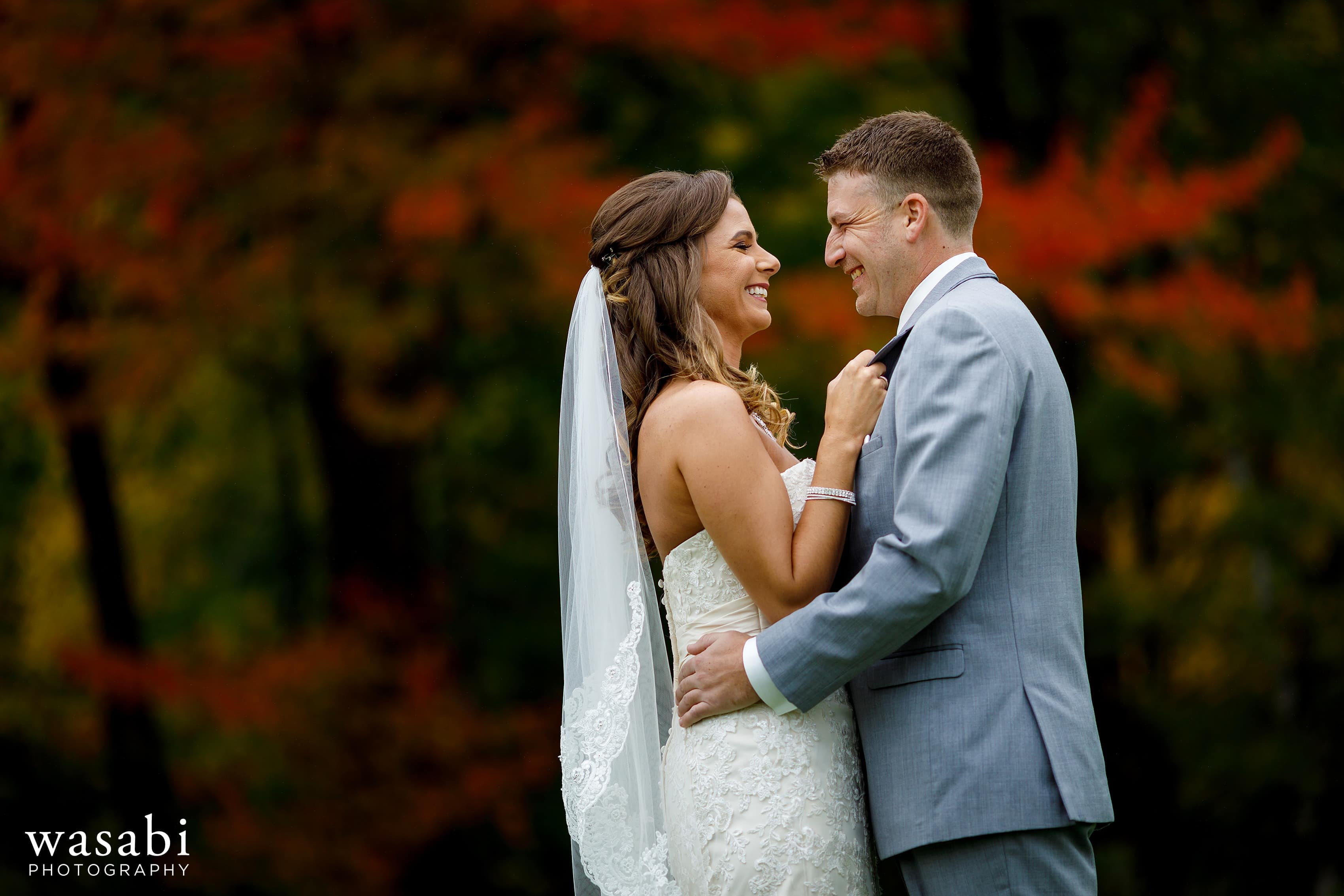 Bride and groom pose for portraits in front of fall color red trees at Buck's Run Golf Club in Mount Pleasant, Michigan.
