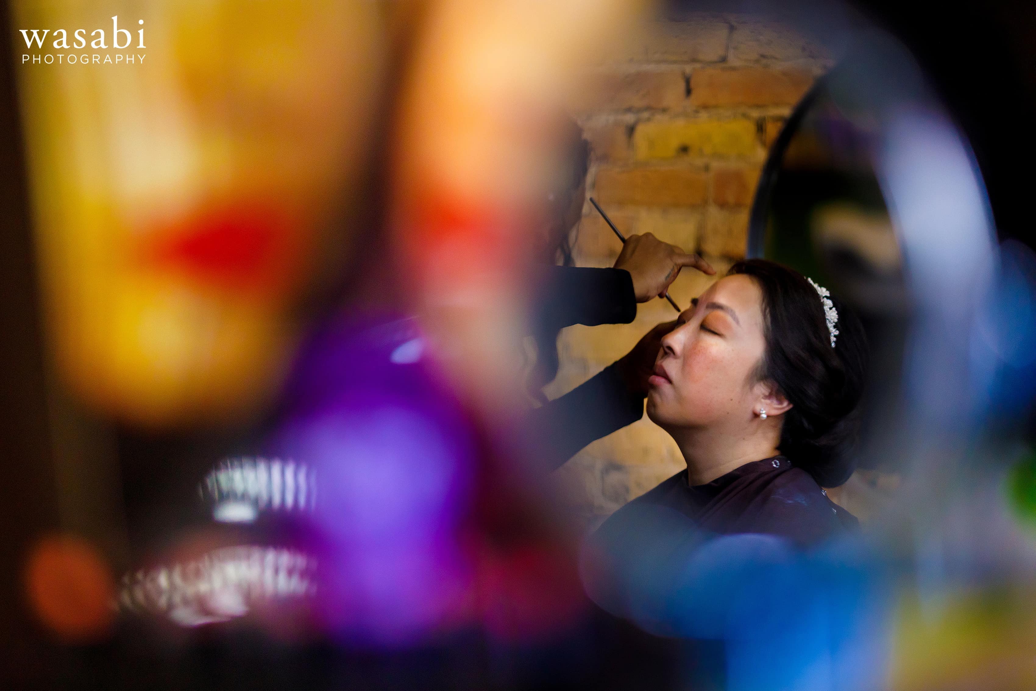 colorful picture of bride having makeup applied at salon before her wedding
