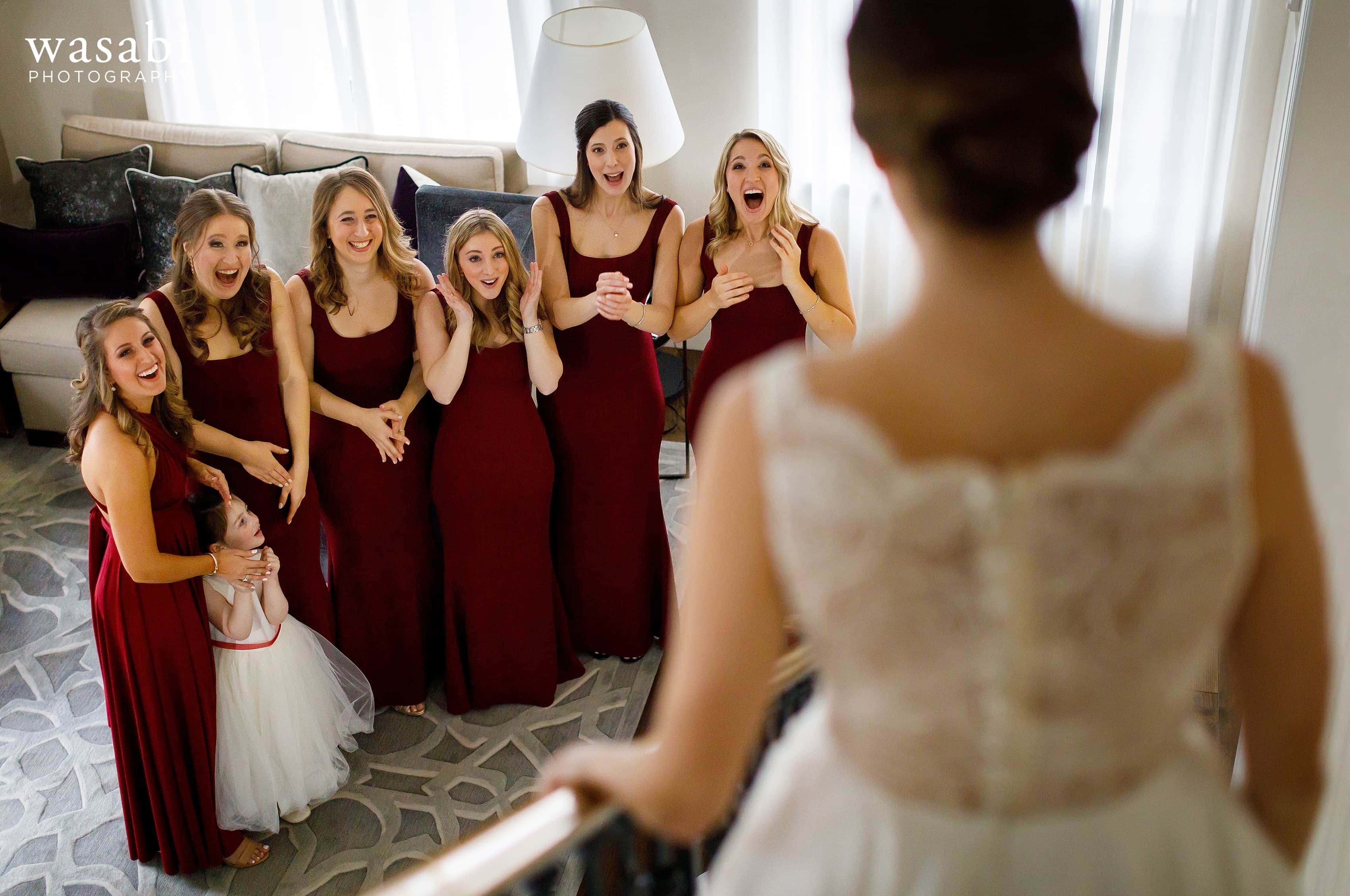 Bridesmaids react to seeing bride in wedding dress walking down the stairs in the presidential suite at InterContinental Chicago Magnificent Mile Hotel