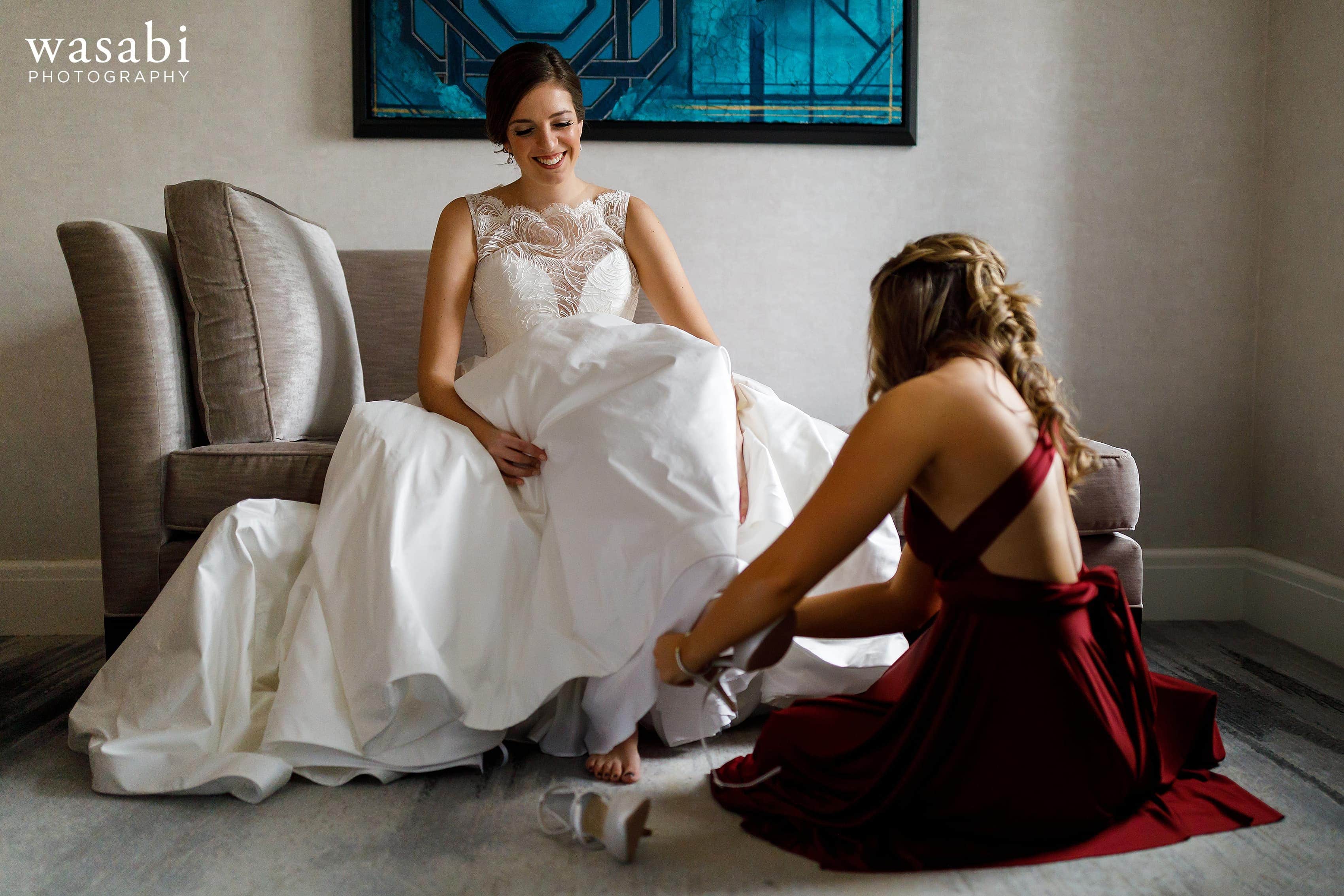 Sister helps bride with shoes while getting ready for wedding in the presidential suite at InterContinental Chicago Magnificent Mile Hotel