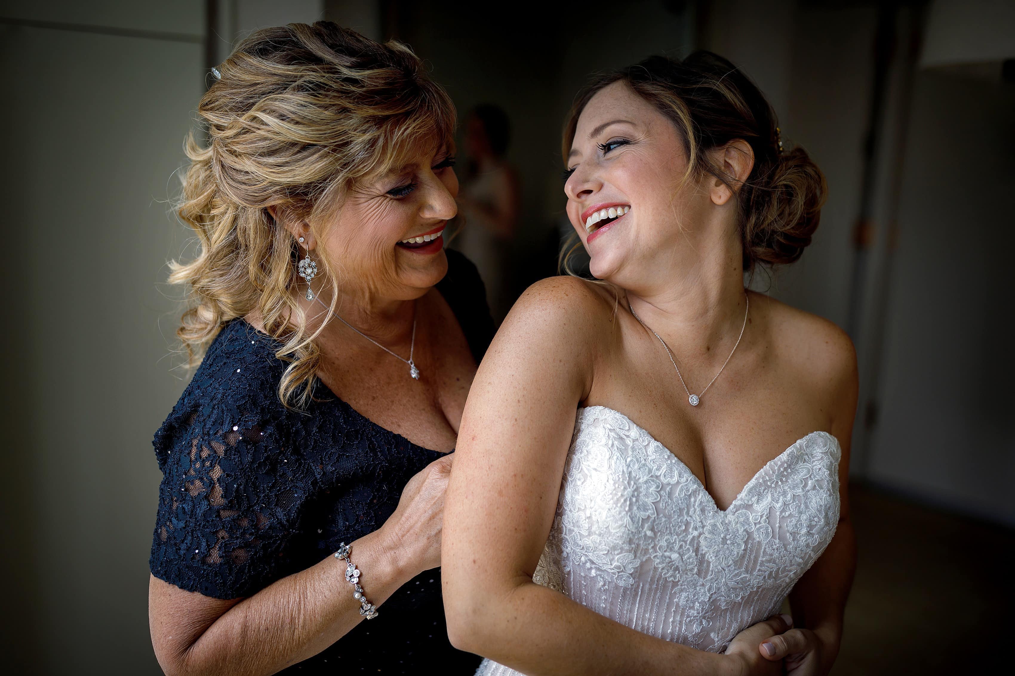 bride and her mother laugh while getting ready before her wedding