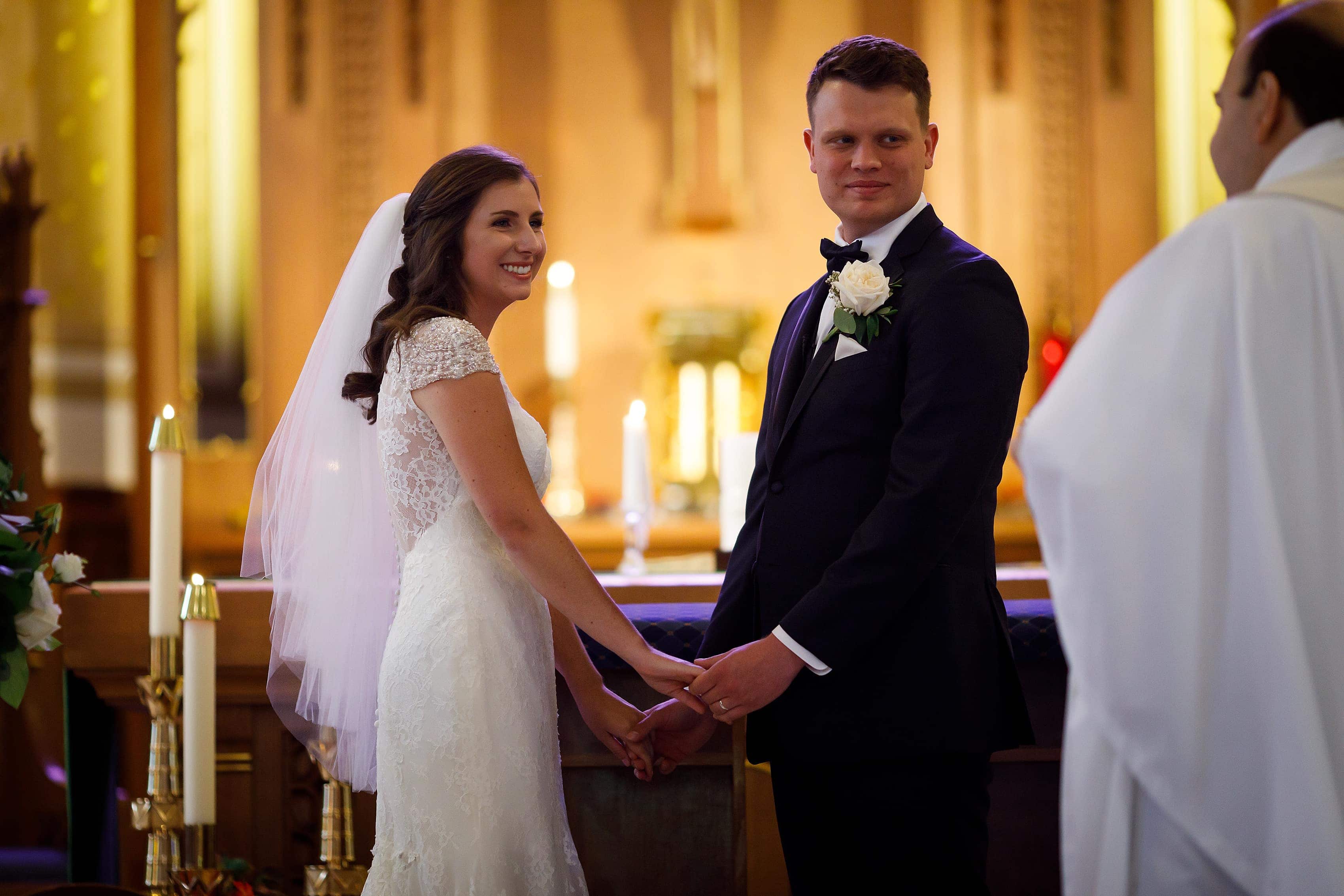 Bride and groom smile at the alter during wedding ceremony at St. Francis Church in Lake Geneva, Wisconsin