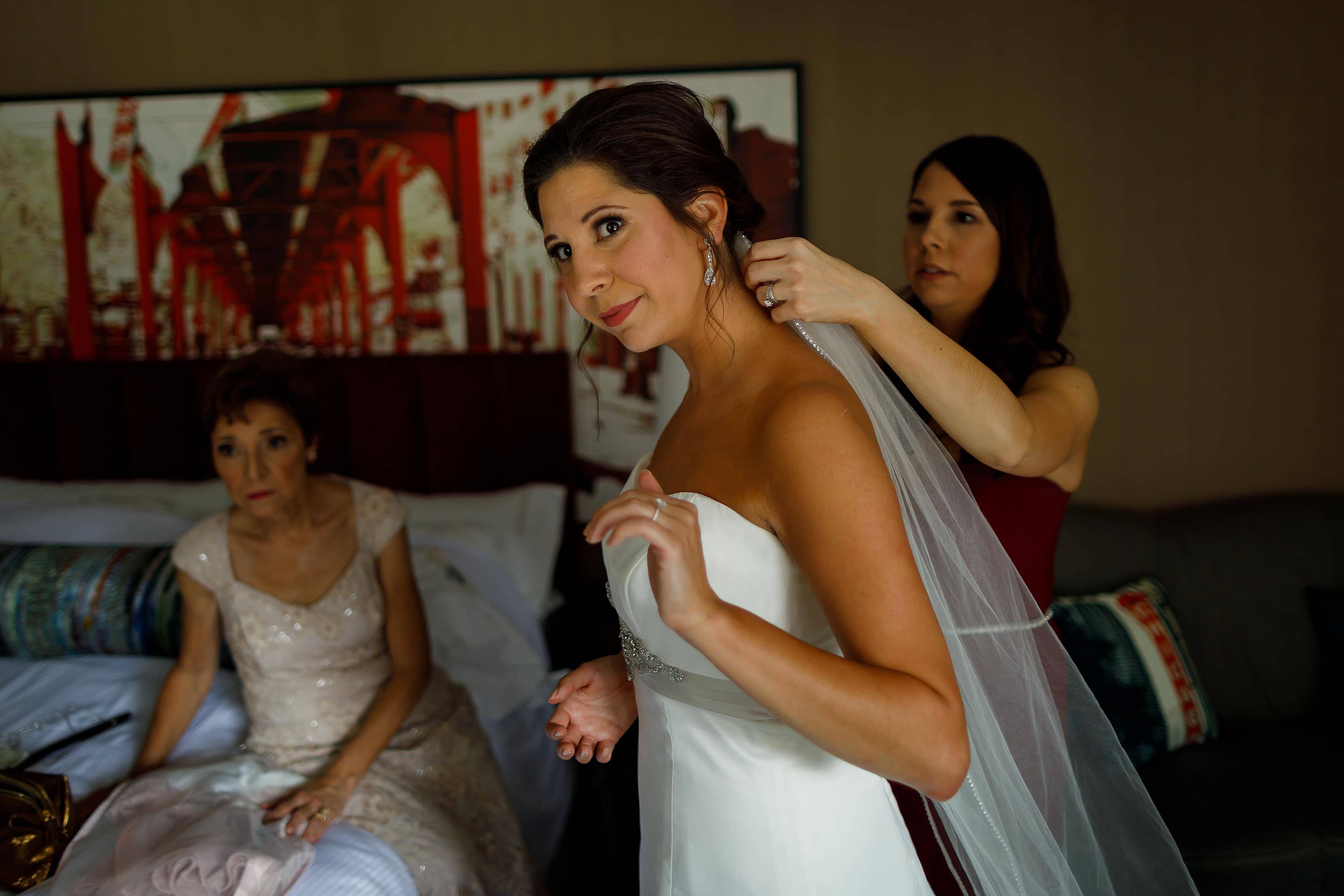 bride puts on veil while getting ready for wedding with her sister and mother