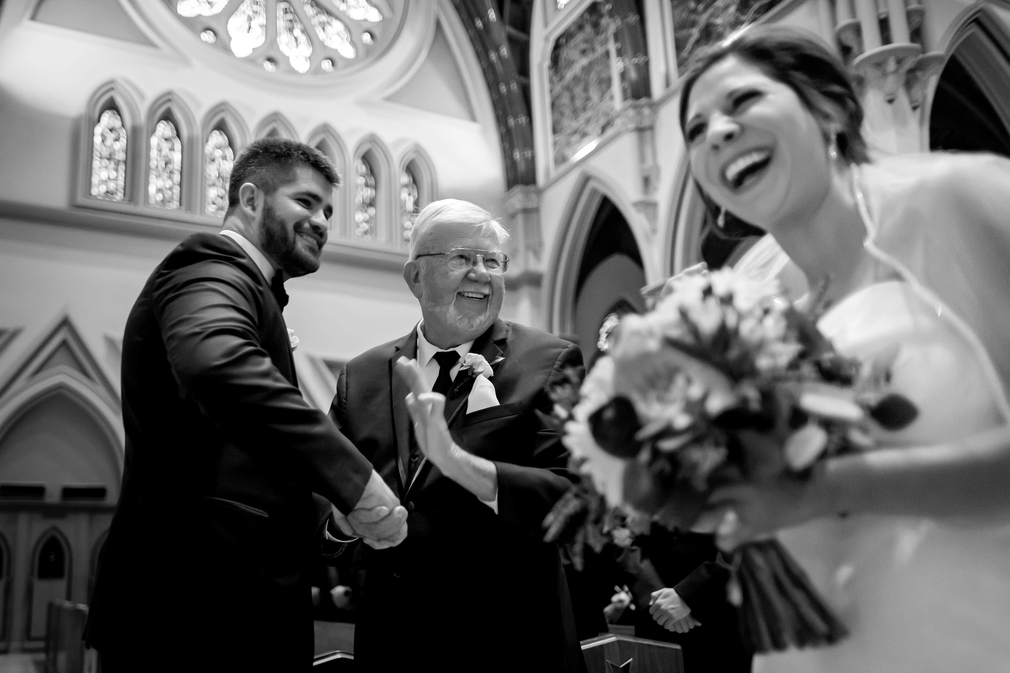 father of the bride shakes hands with the groom while bride laughs during wedding at Holy Name Cathedral in downtown Chicago