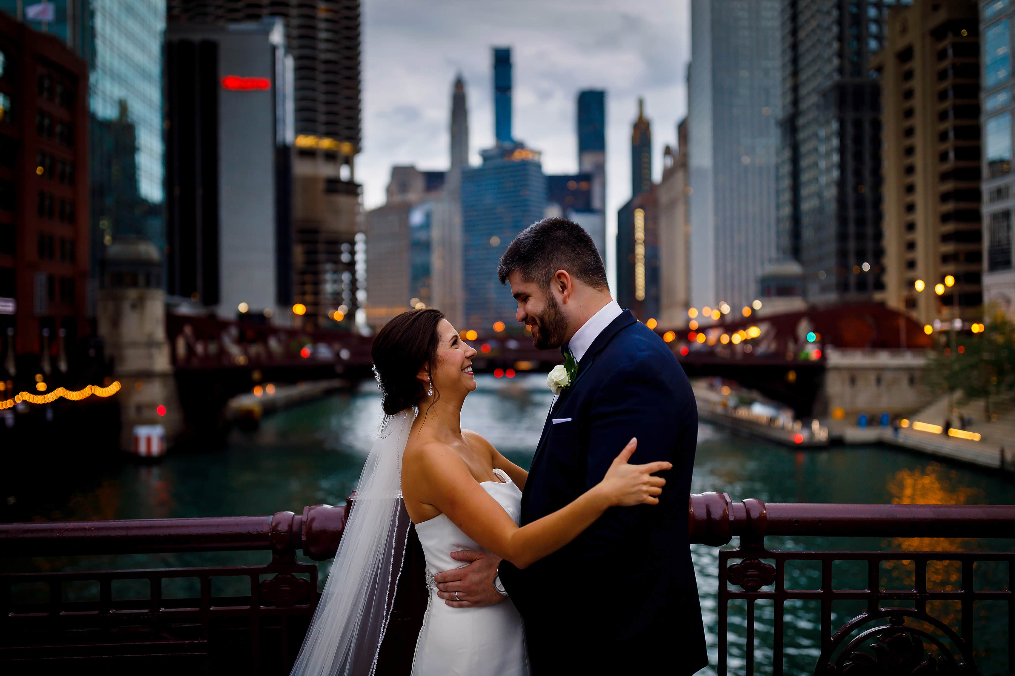 bride and groom pose for wedding photos on LaSalle Street bridge in downtown Chicago with river and skyline in the background