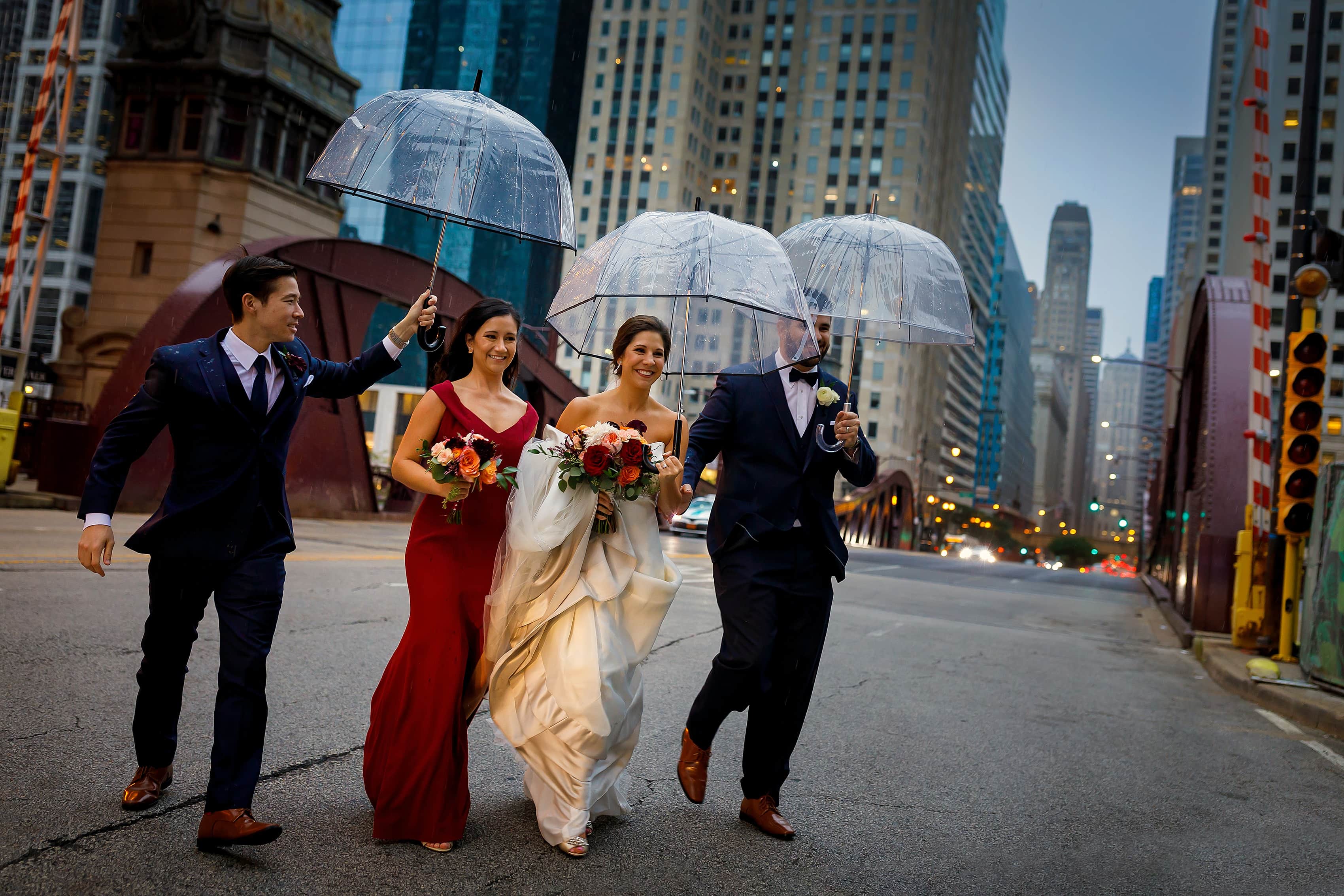 bride and groom walk across LaSalle Street with umbrellas as rain starts during wedding in downtown Chicago