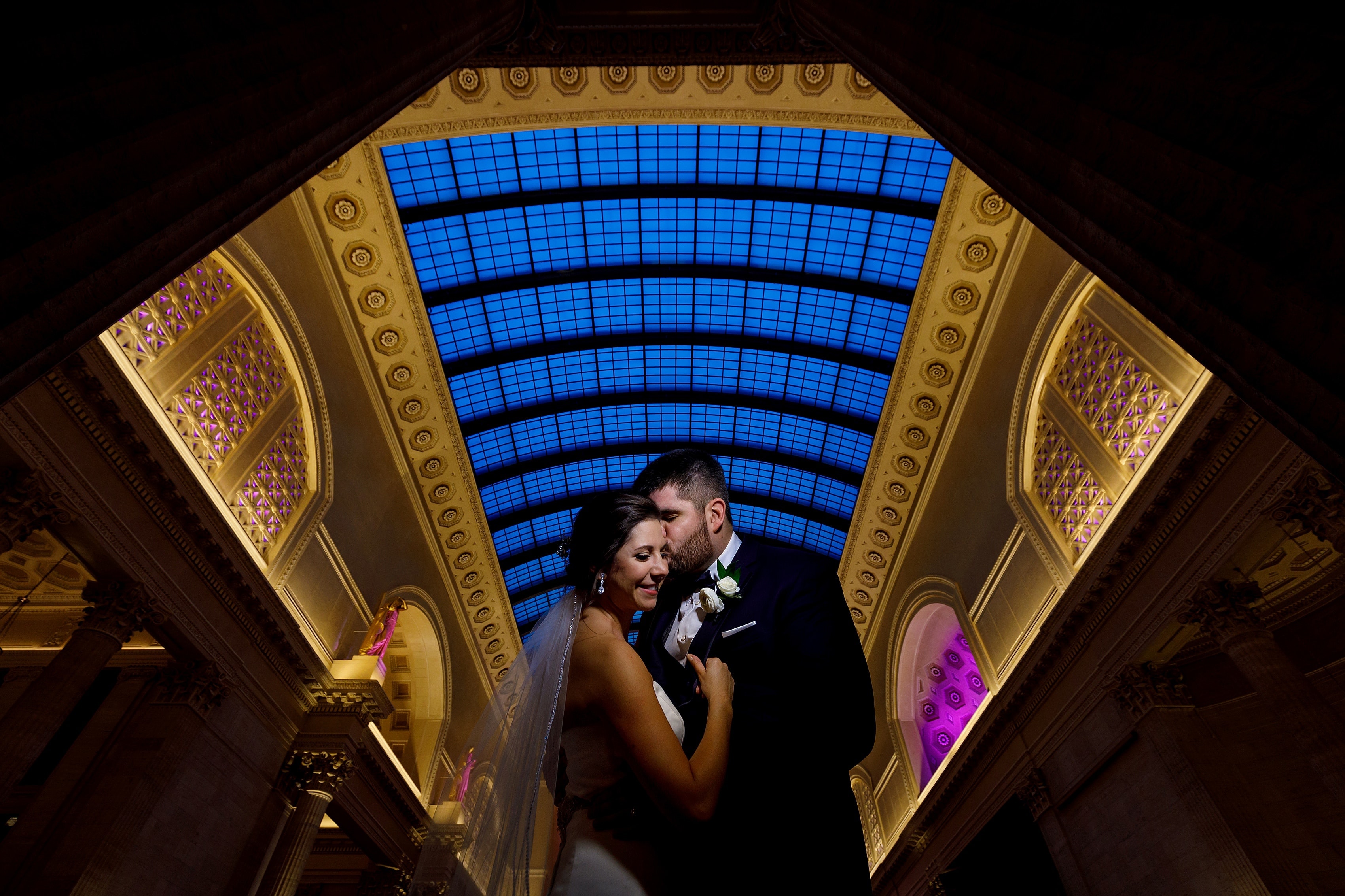 bride and groom pose for wedding photos inside Union Station during wedding in downtown Chicago with glass ceiling featured prominently 