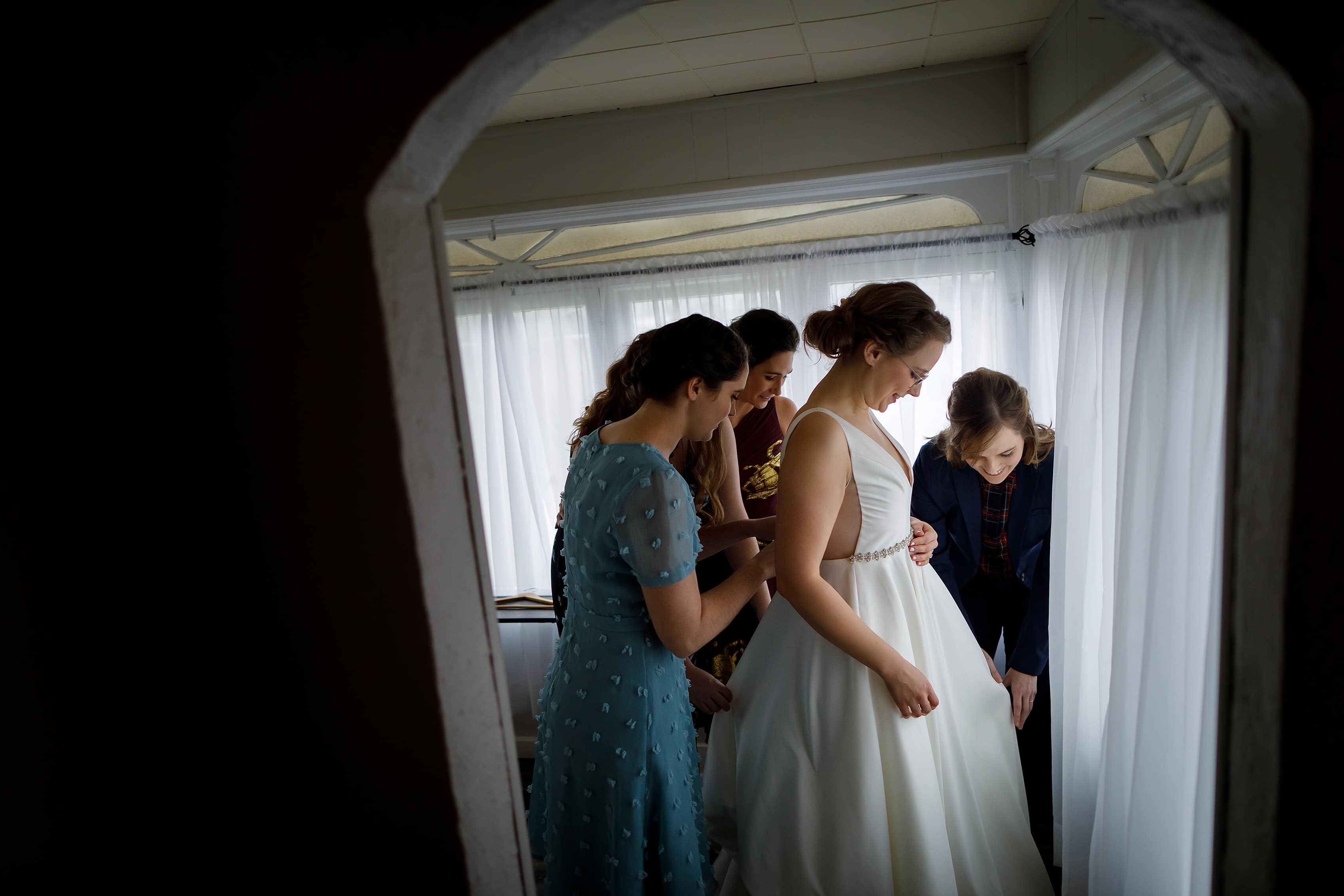 bridesmaids help bride into wedding dress