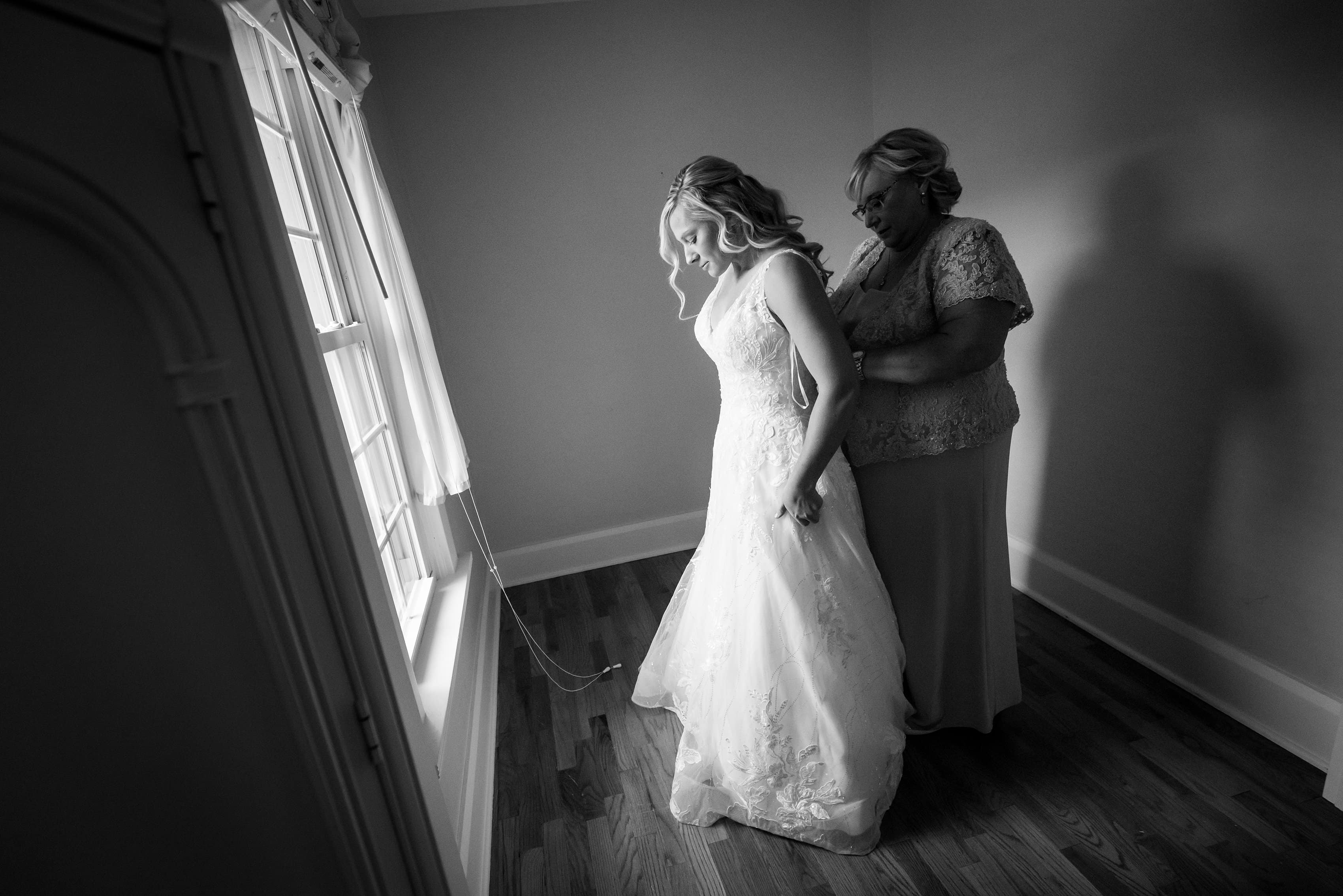 mother of bride helps daughter into wedding dress