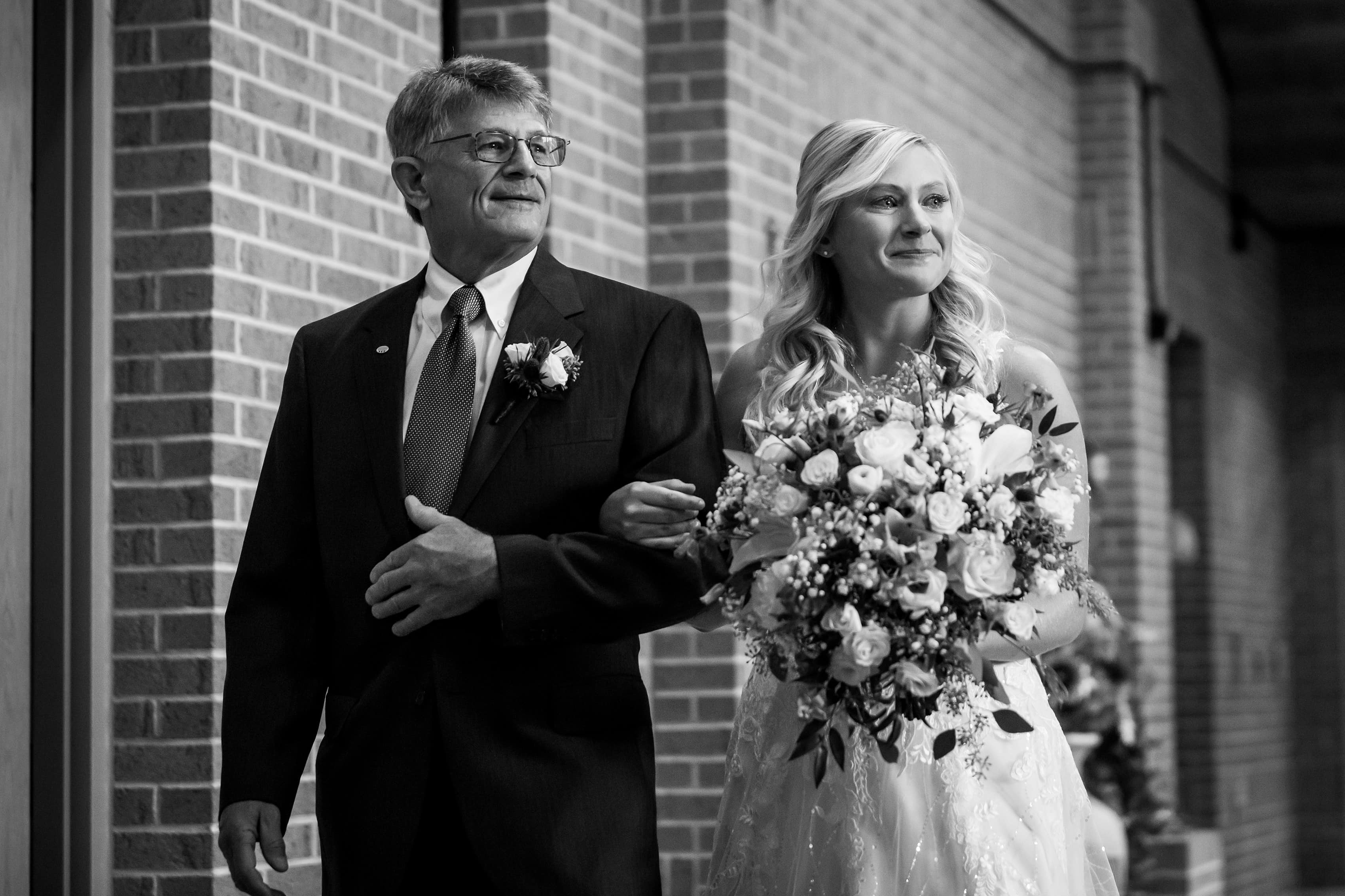 Bride walks down the aisle with her father during wedding ceremony at Cross in the Woods in Indian River, Michigan