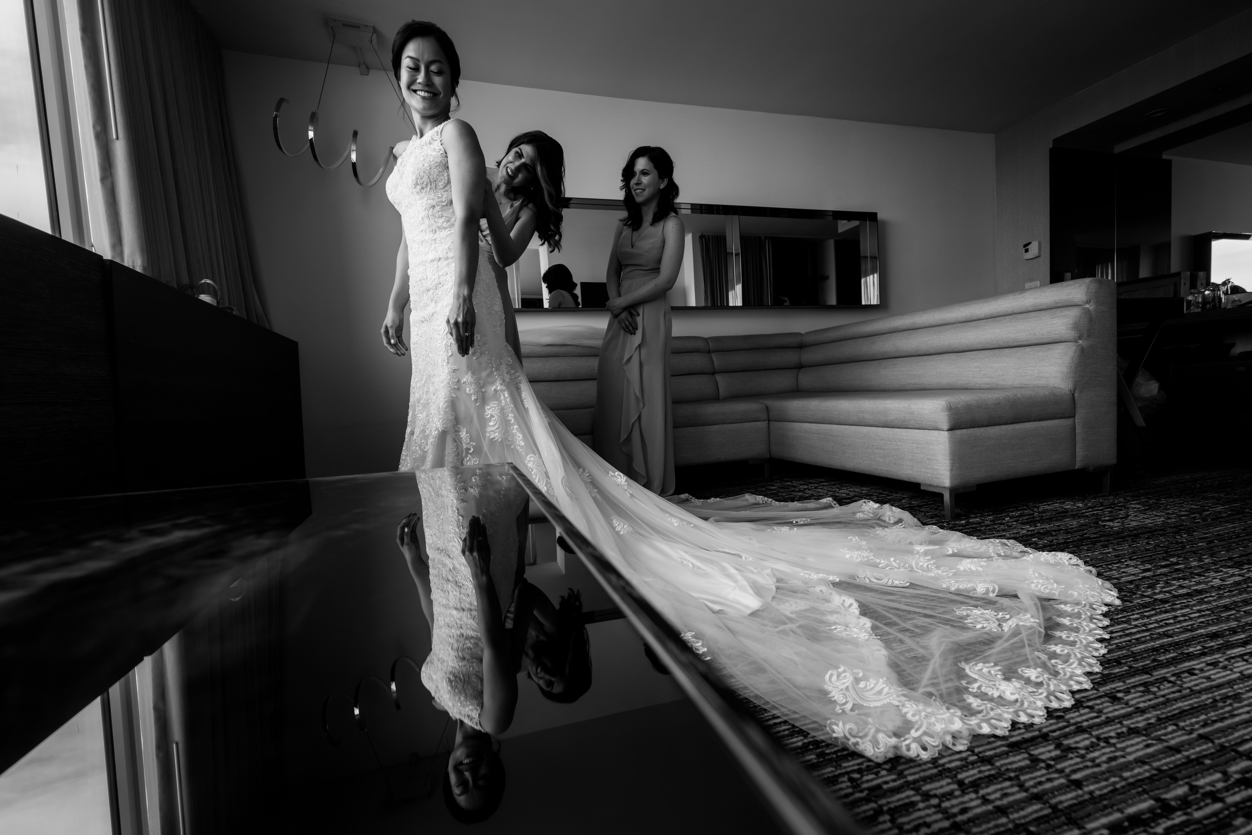 Bridesmaids help bride with dress while getting ready for her wedding in a hotel suite