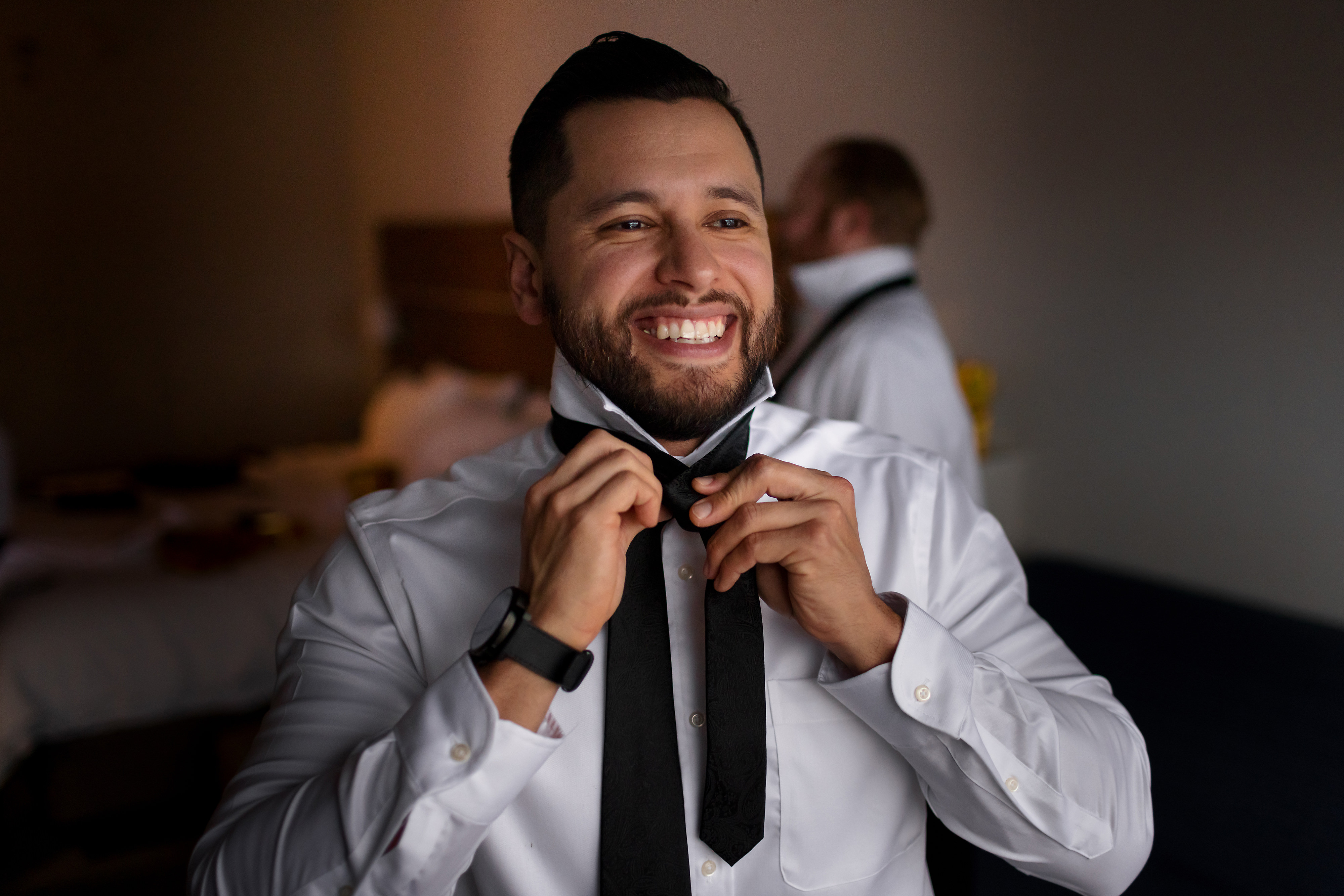 Groom puts on tie while getting ready for wedding