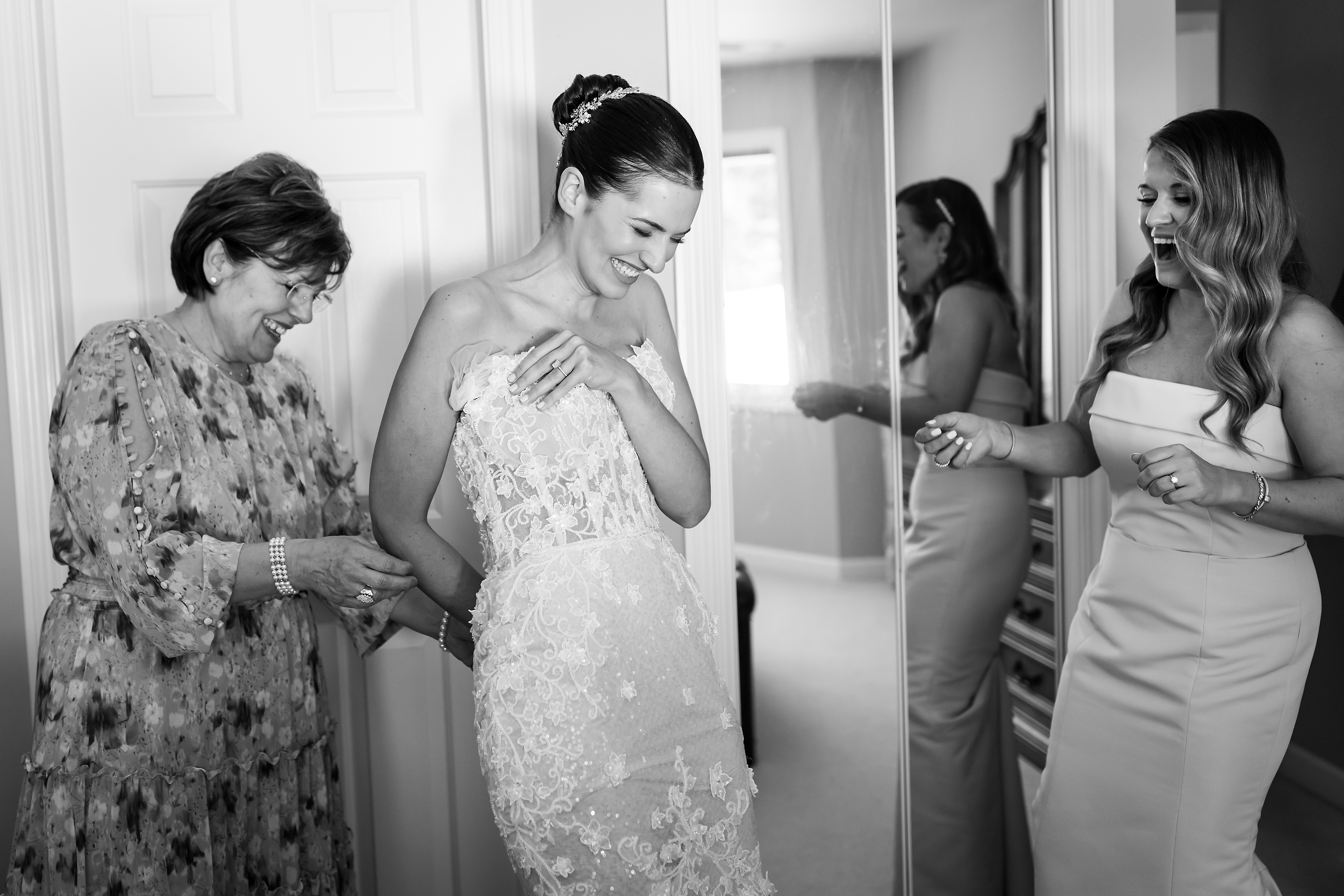 Mother and bridesmaid help bride put on wedding dress