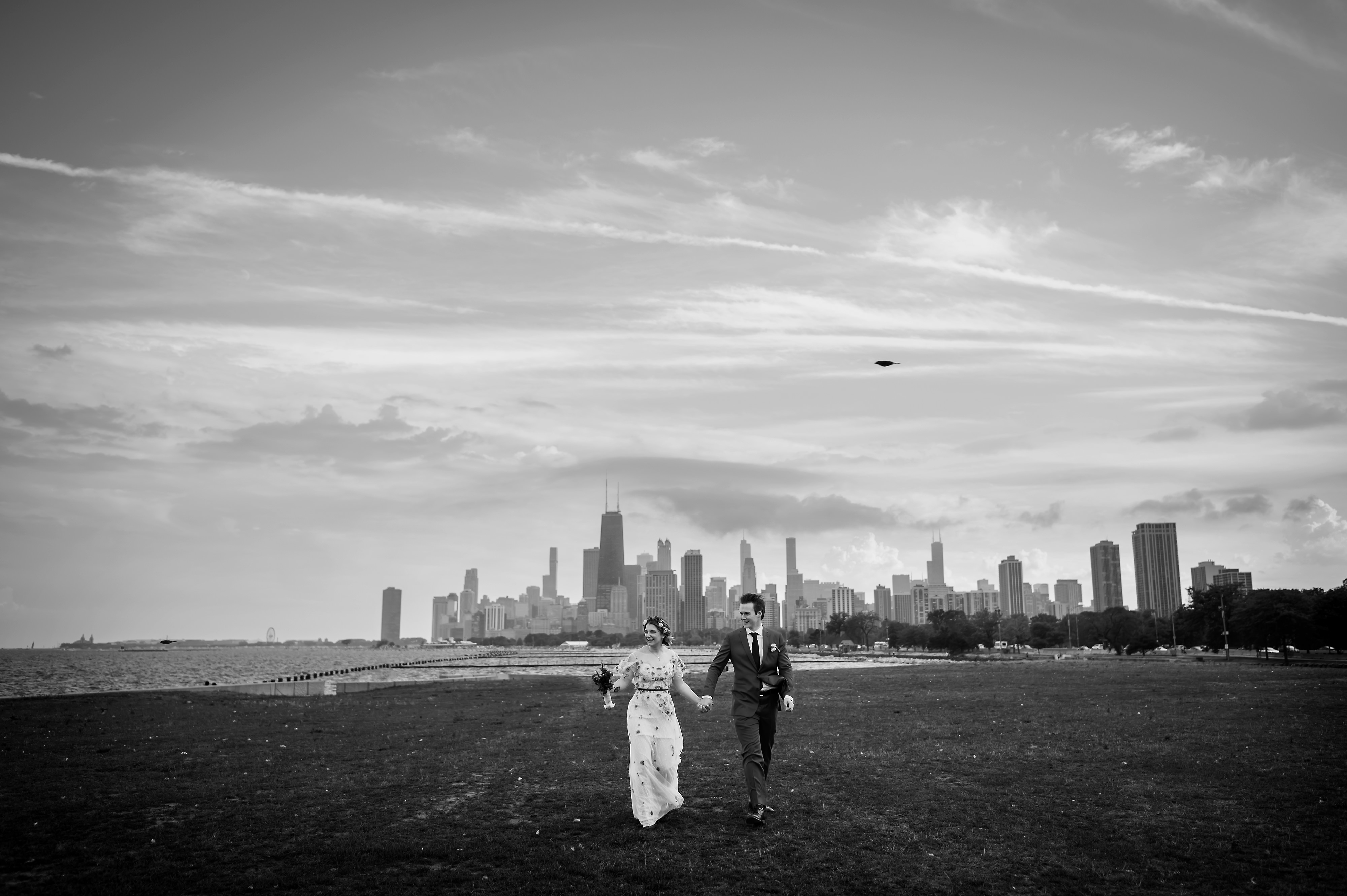 bride and groom walk together at Fullerton Beach with the Chicago Skyline in the background on their wedding day