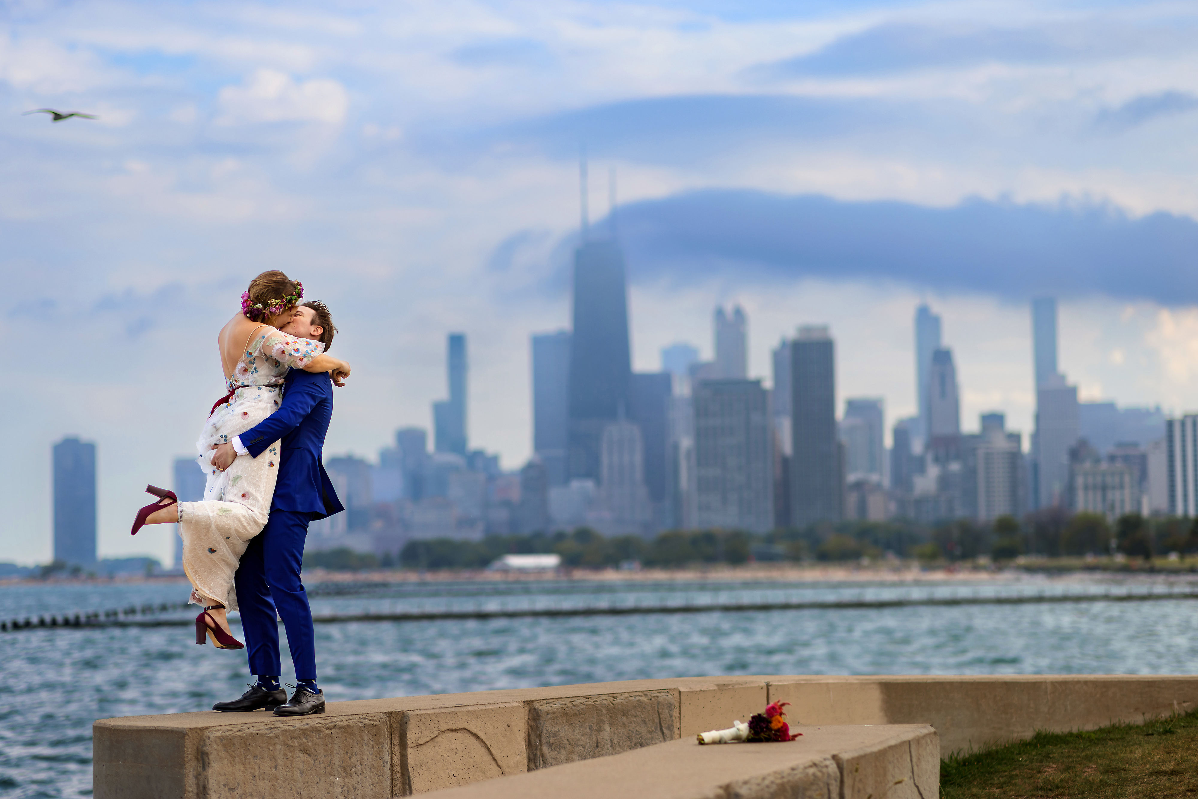 bride and groom kiss on the break wall at Fullerton Beach with the Chicago Skyline in the background on their wedding day