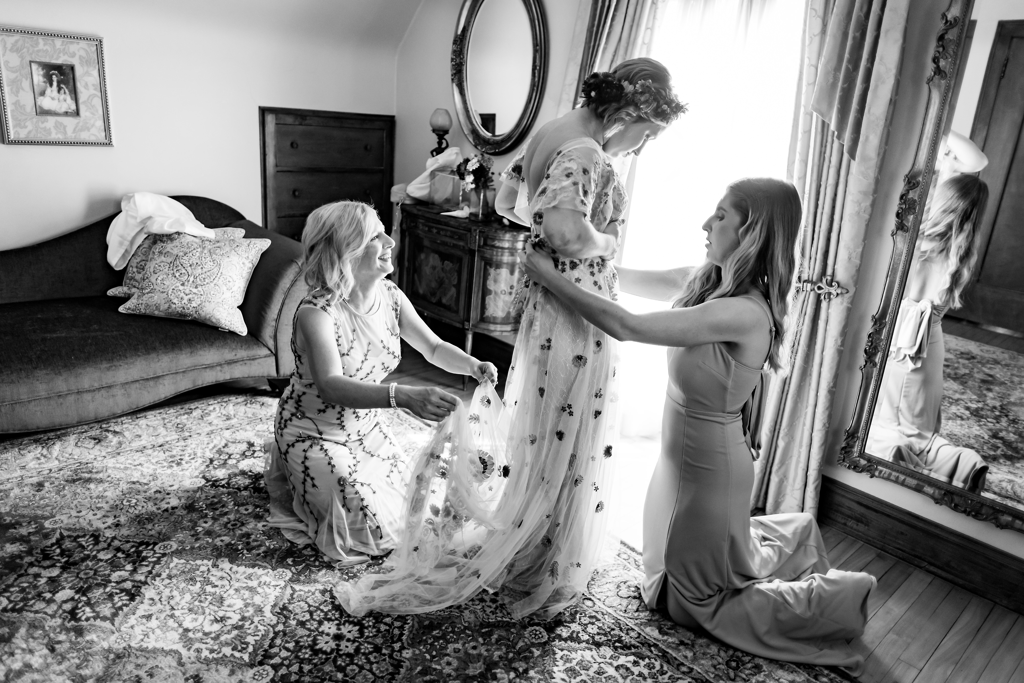 mother and maid of honor help bride put on dress while getting ready for wedding at The Grove Redfield Estate in Glenview