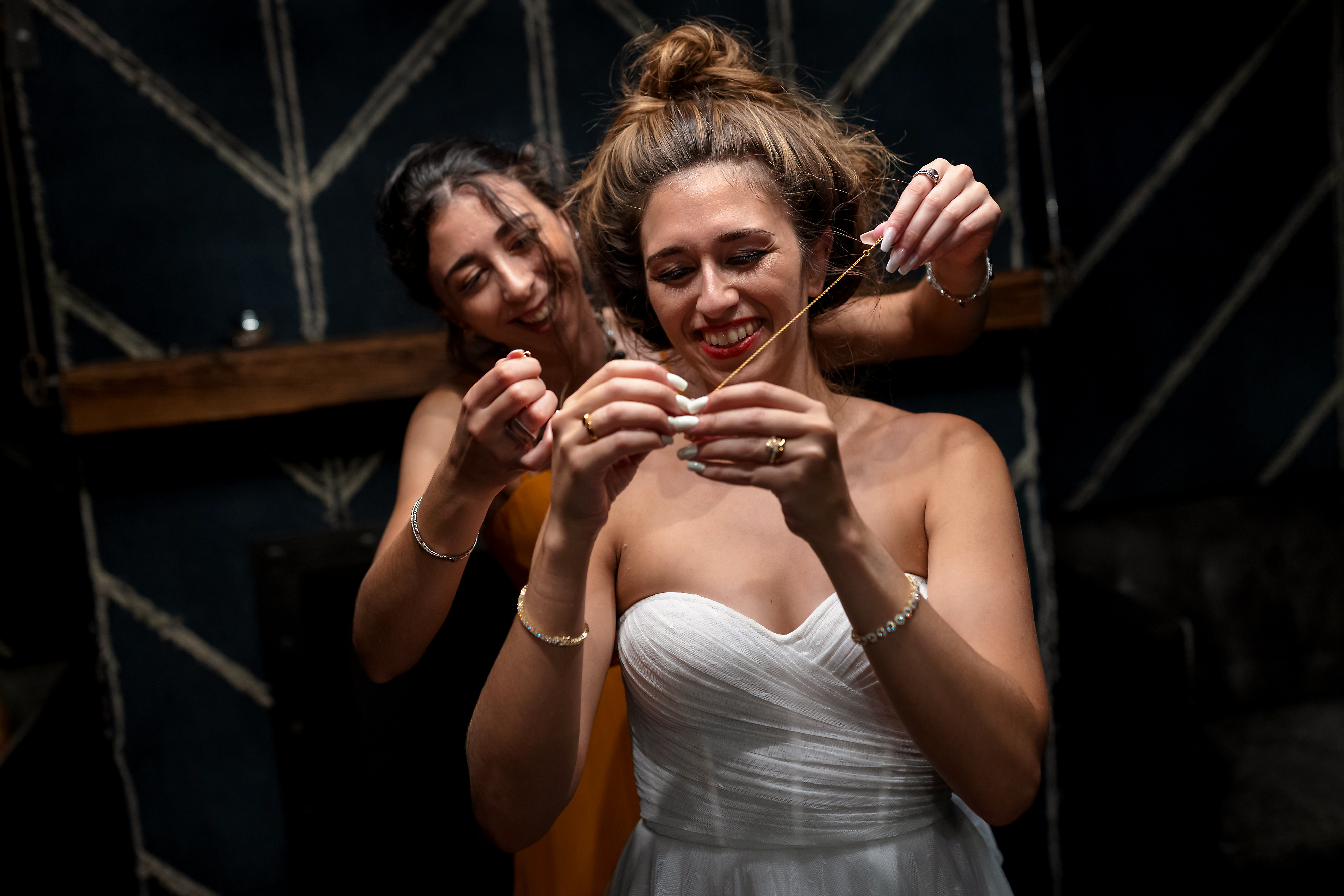 Sister helps bride put on necklace while changing outfits before first dance during wedding reception at The Dawson restaurant in downtown Chicago