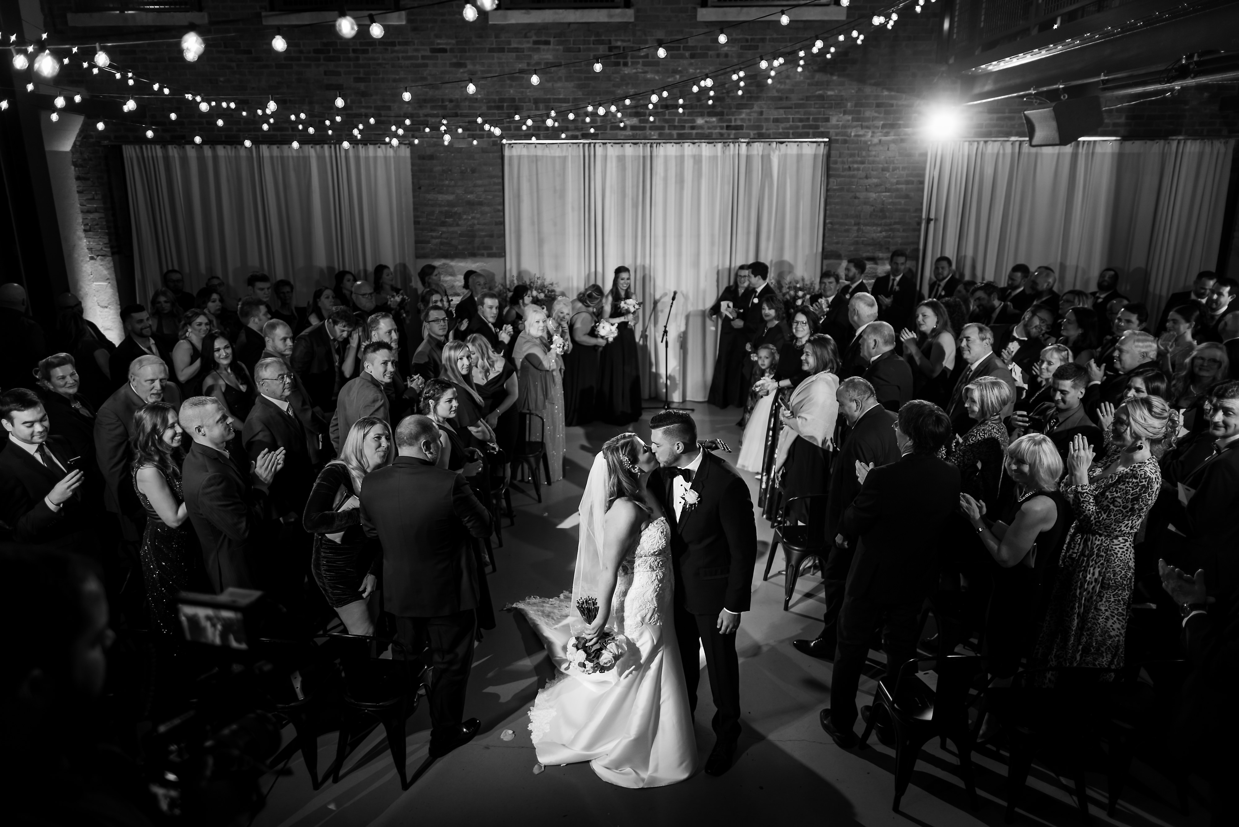 Wide angle view of couple kissing in North Atrium ceremony space with candles and chandeliers during wedding ceremony at Artifact Events in Chicago's Ravenswood neighborhood.