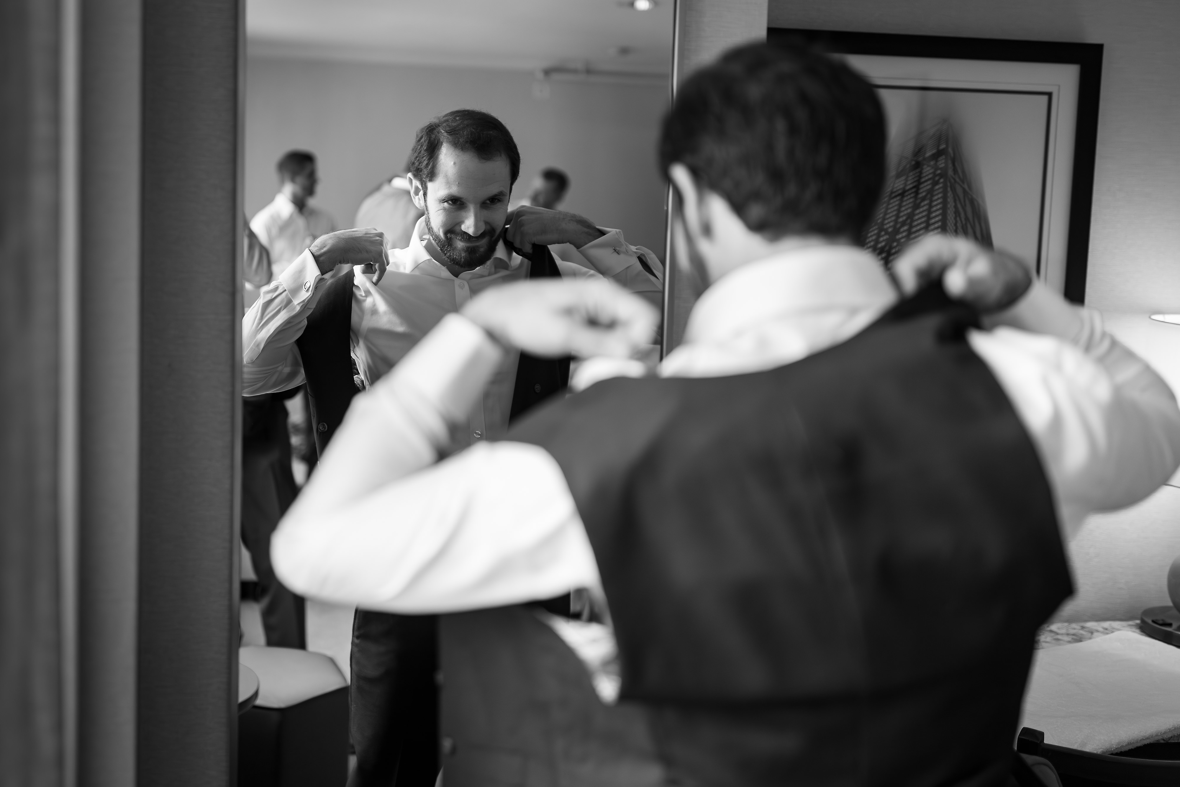 Groom looks into mirror while putting on vest for his wedding in Lincoln Park, Chicago