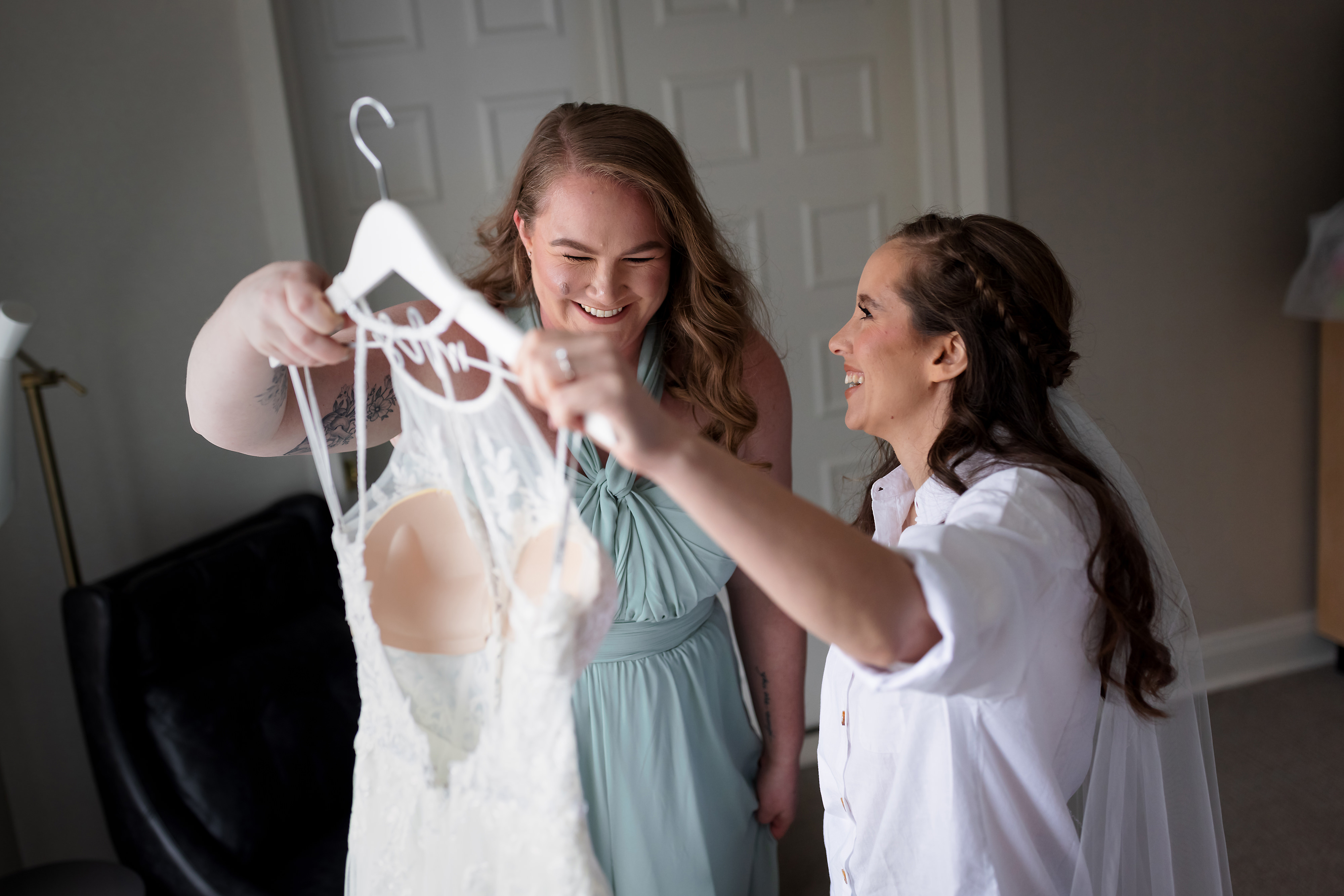 Bride and maid of honor get dress off wall while getting ready for wedding