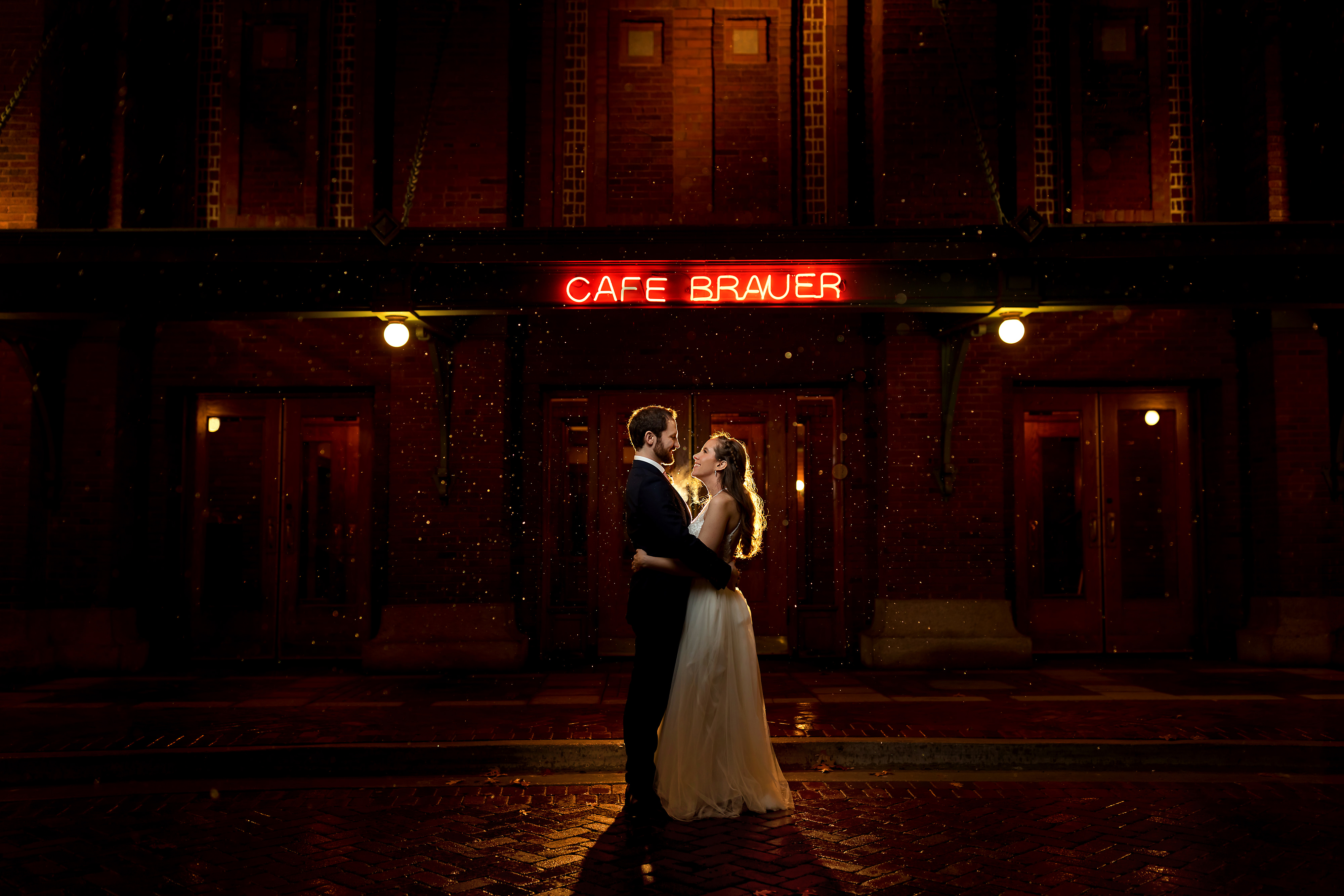 backlit portrait at night in the rain of bride and groom outside in front of neon lights at Cafe Brauer in Chicago's Lincoln Park neighborhood during their wedding reception