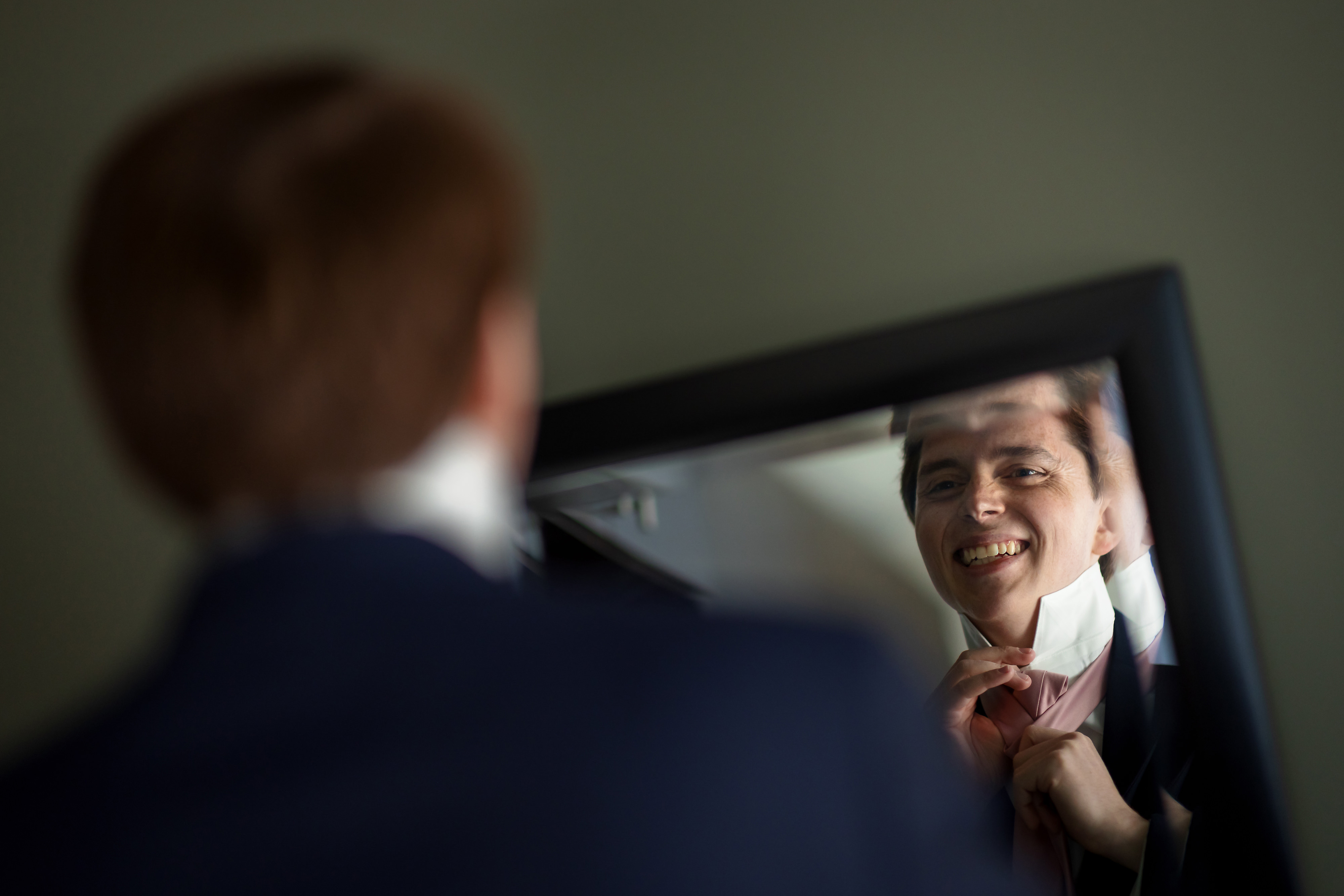 groom looks in mirror while tying tie