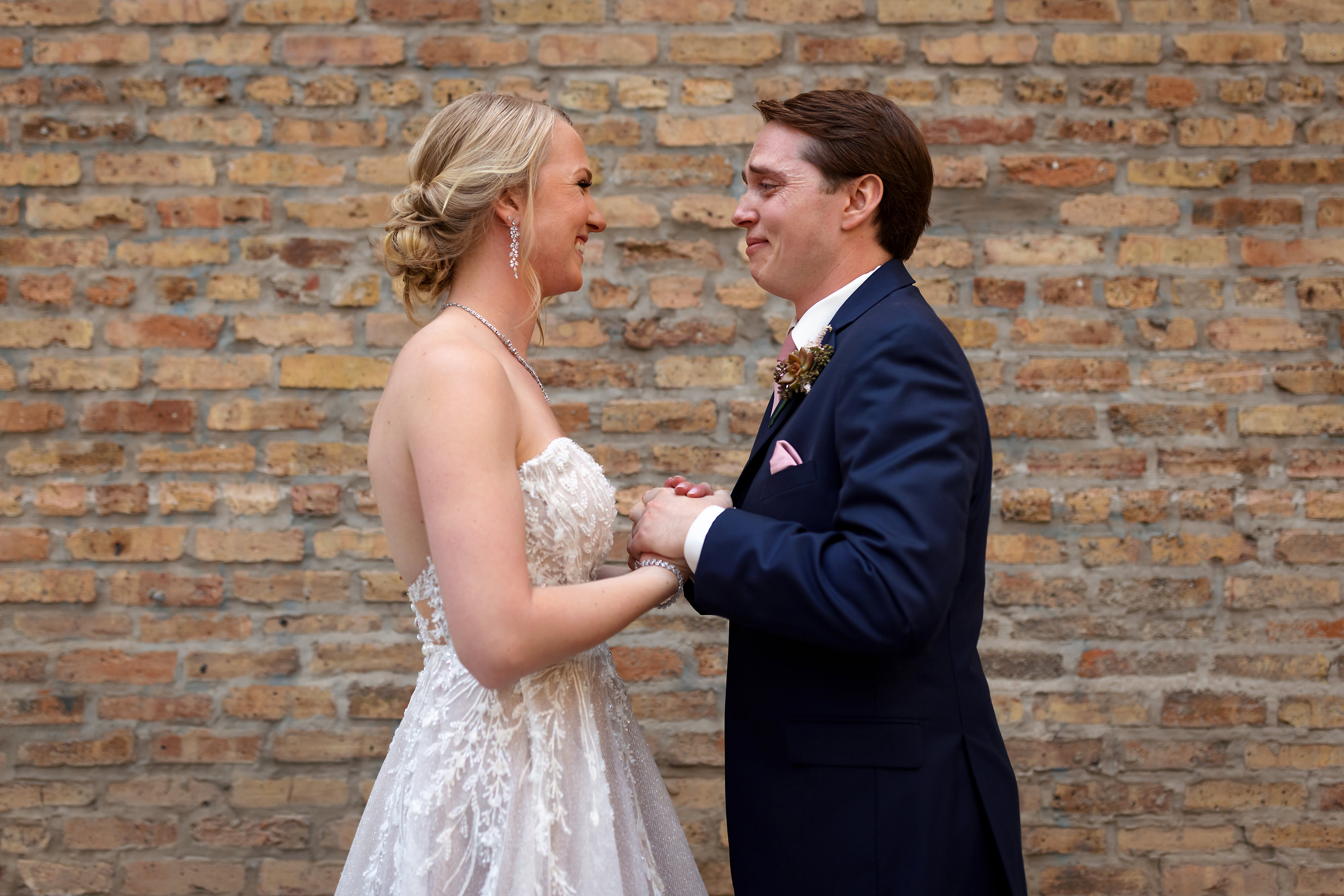 Bride and groom react during first look with brick background