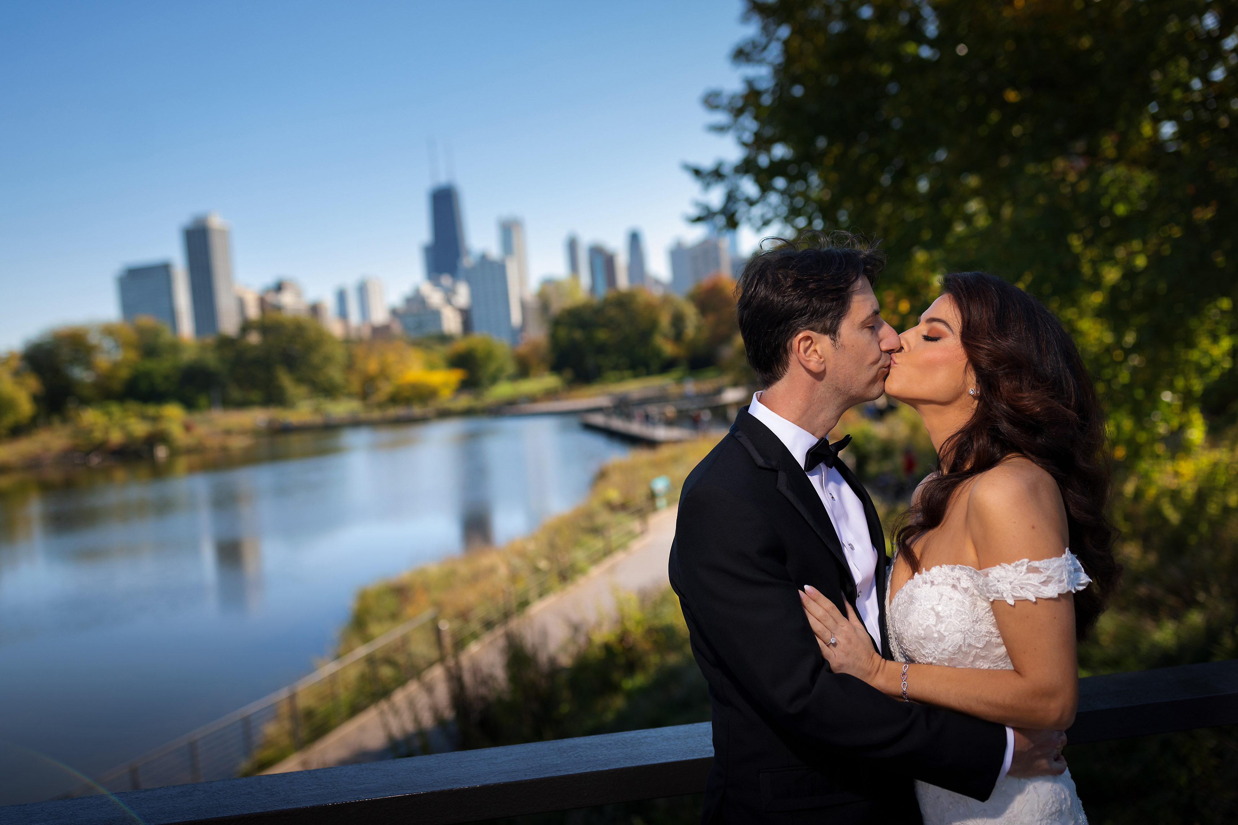 Bride and groom kiss on the bridge over looking Lincoln Park's South Pond and the Chicago skyline
