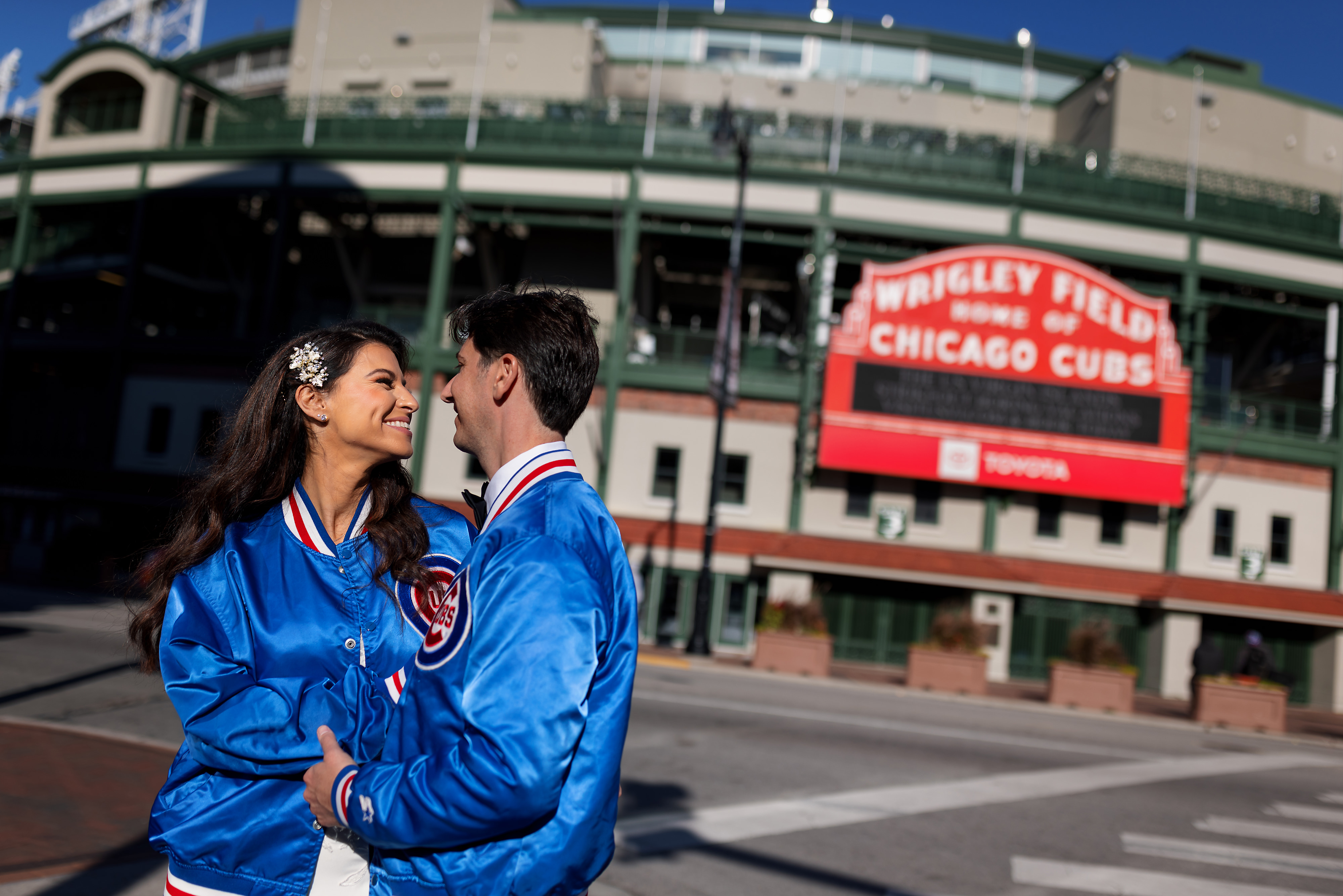 Bride and groom pose for portrait in Cubs jackets outside Wrigley Field in Chicago