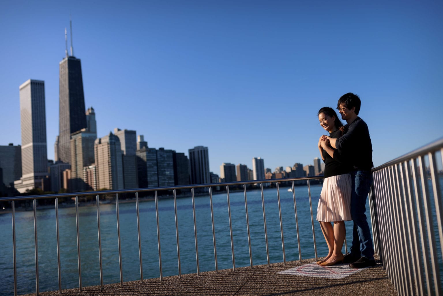 couple poses for engagement photos at milton lee olive park in chicago with lake michigan and the skyline in the background